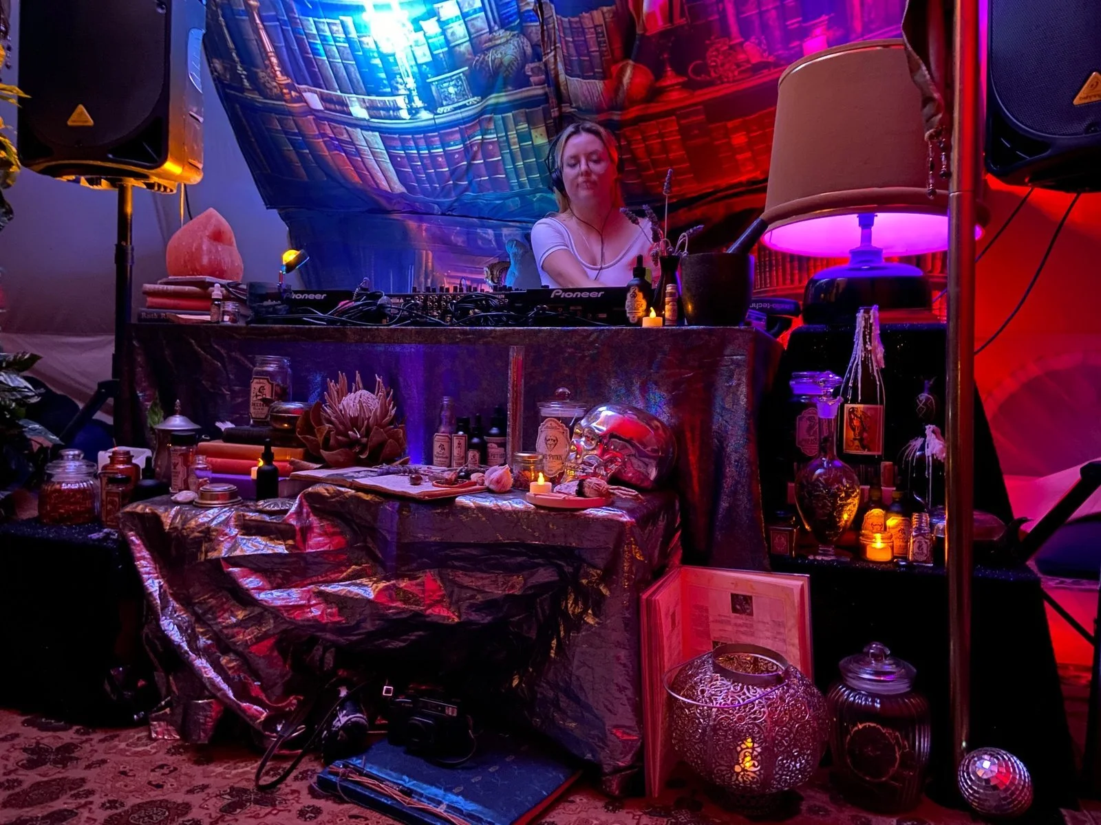 A female DJ is performing at a colorful, mystical-themed event, surrounded by various Leisure Disco Decor decorative items, candles, and ambient lighting.