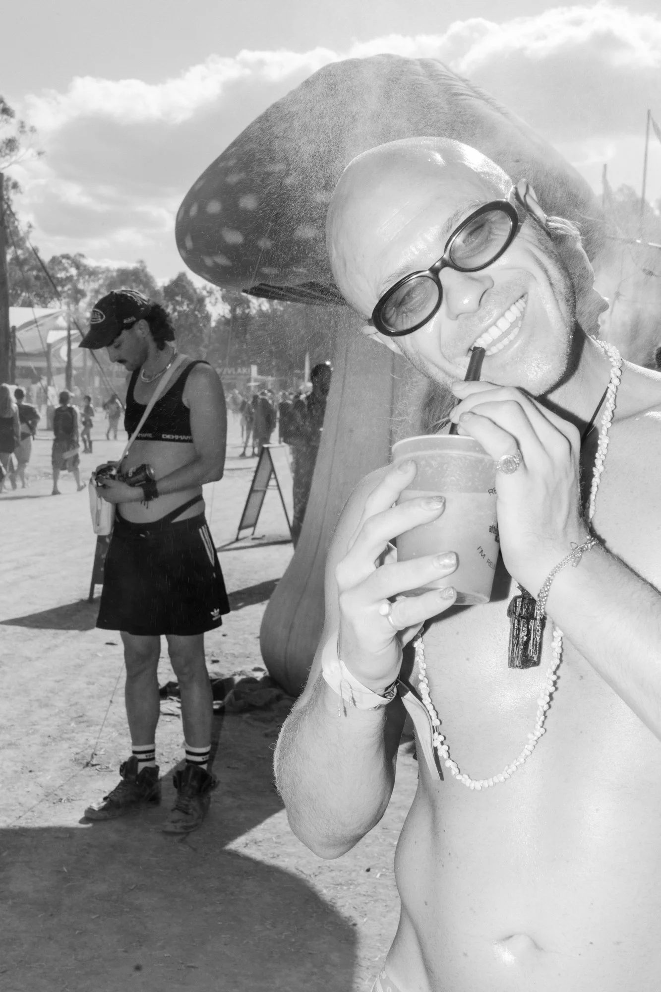 A person smiling through a glass window at a festival, holding a cup and straw, with a large sombrero hat on the roof of a booth.