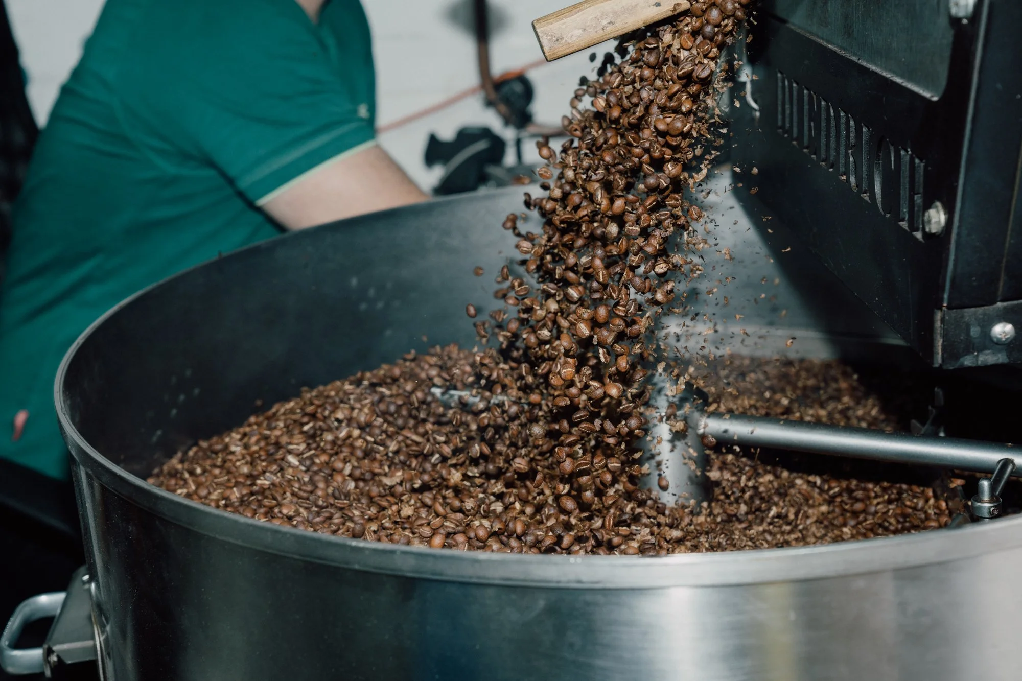 Roasted coffee beans falling into a large metal container from a machine.