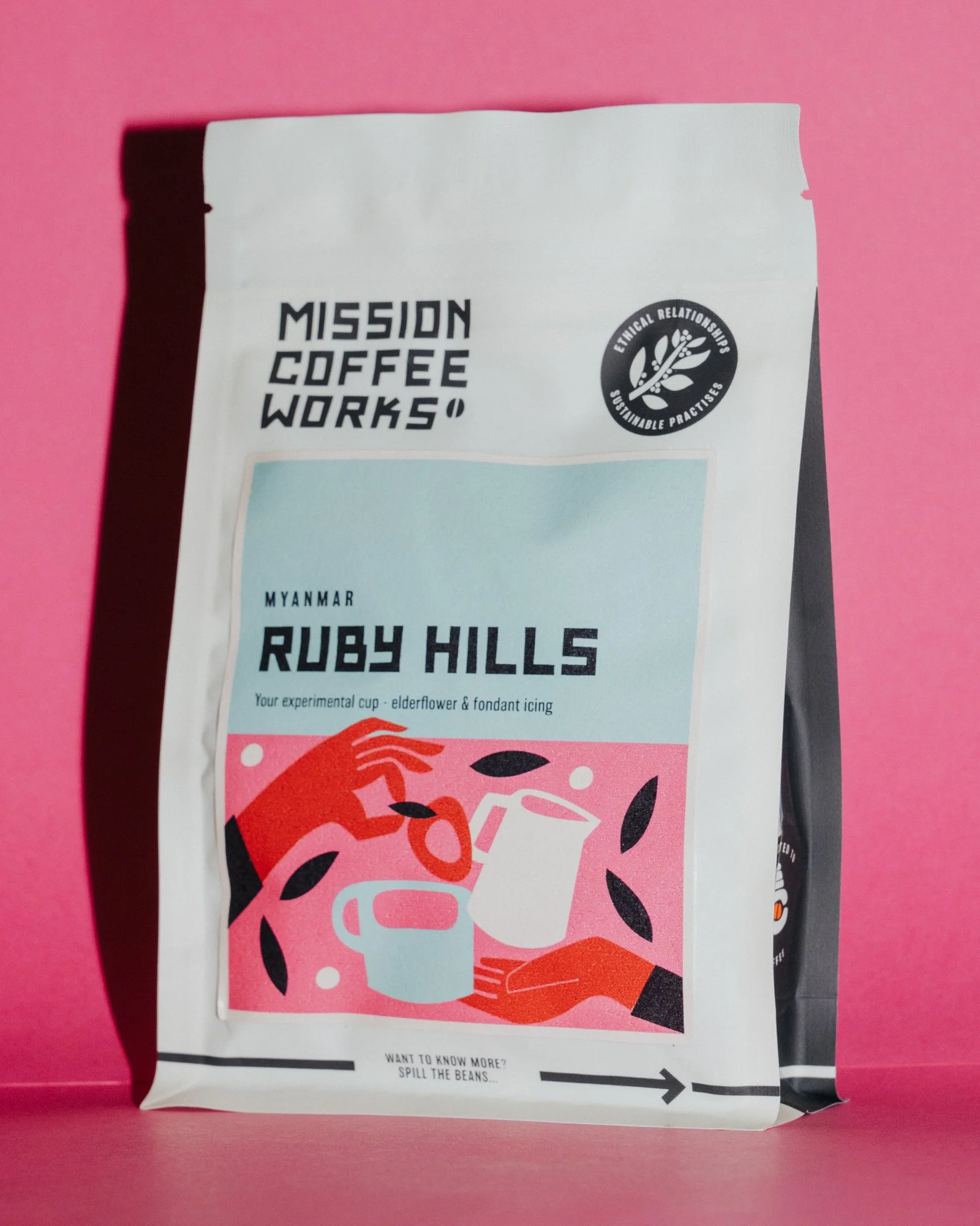 Coffee package from Mission Coffee Works labeled Myanmar Ruby Hills with illustration of two hands sharing a cup on pink background