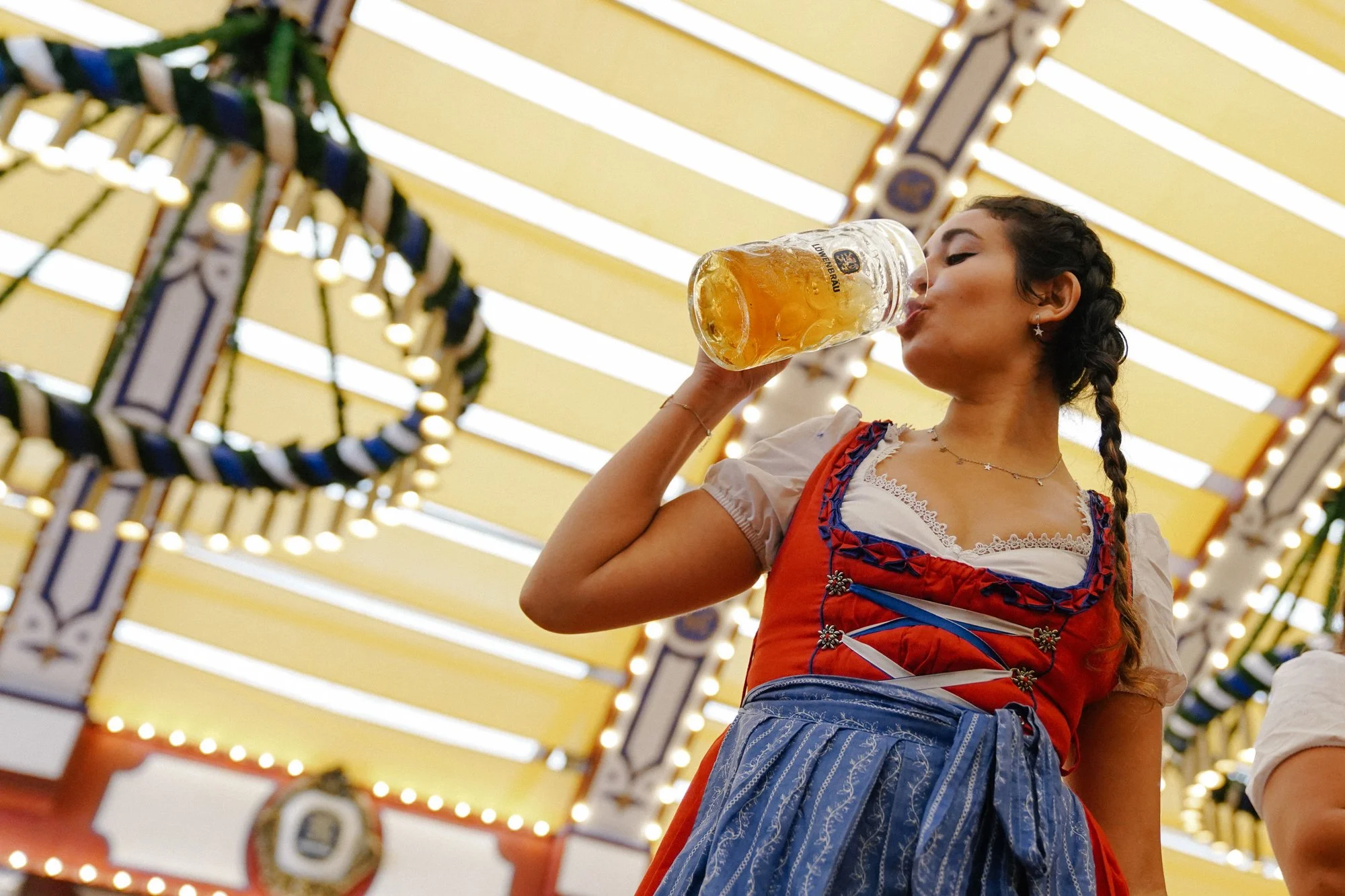 Woman dressed in traditional Bavarian dirndl drinking beer at Oktoberfest.