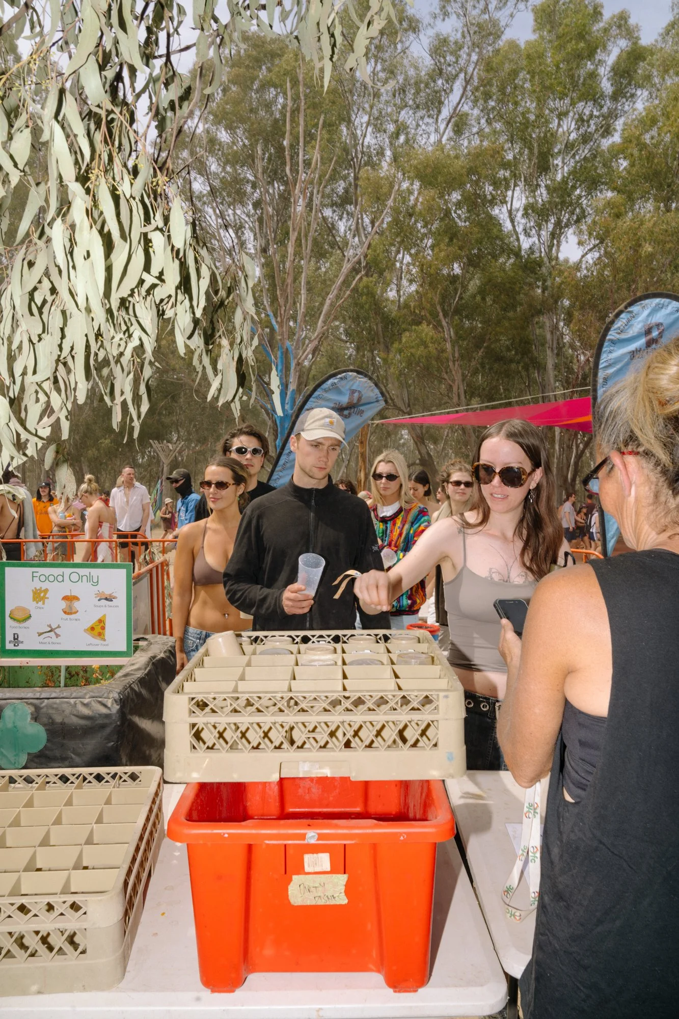 People in line at an outdoor food stall with a sign reading "Food Only" and containers of food on the table.