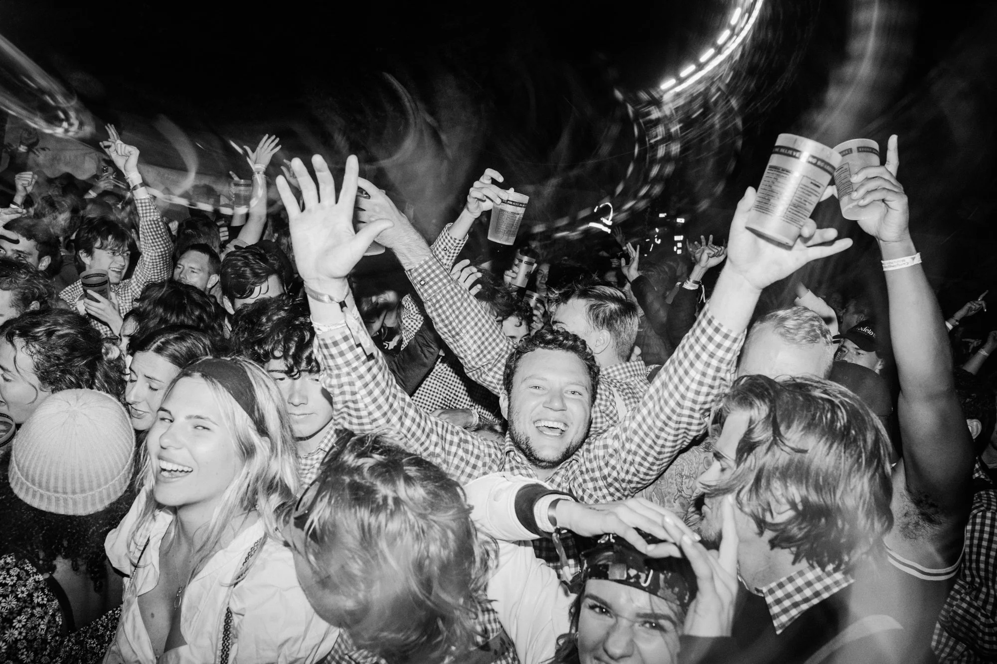 Crowd of people dancing and celebrating at a night event, with some holding cups, in a lively environment.