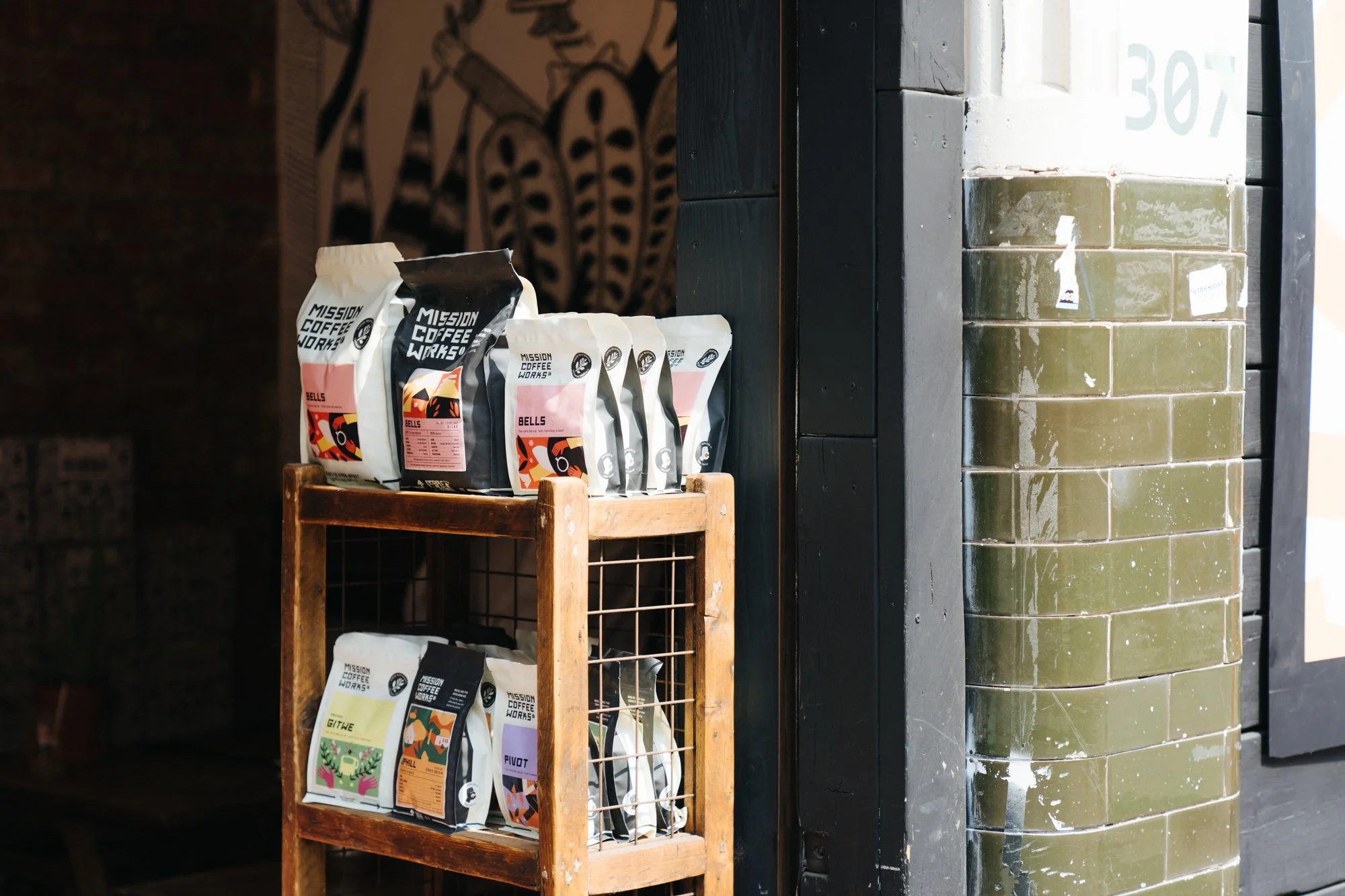 Bags of Mission Coffee Works on a small wooden shelf inside a cafe.