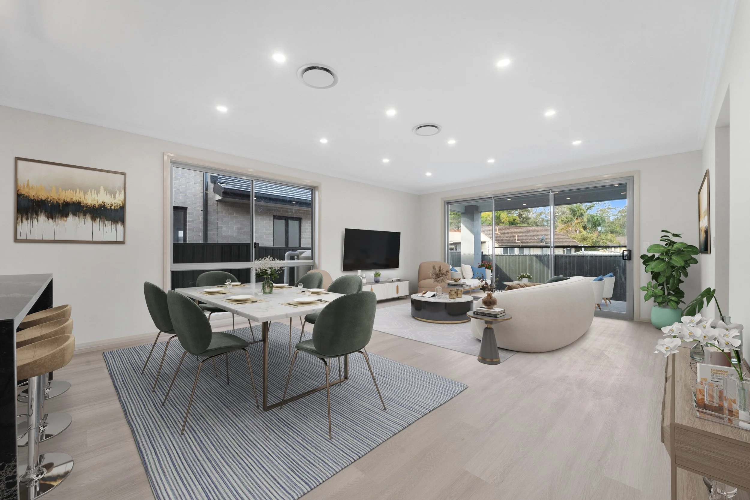 Living room with dining table, six chairs, sofa, armchair, coffee table, TV, large windows, art on walls, potted plants, on light wood flooring.
