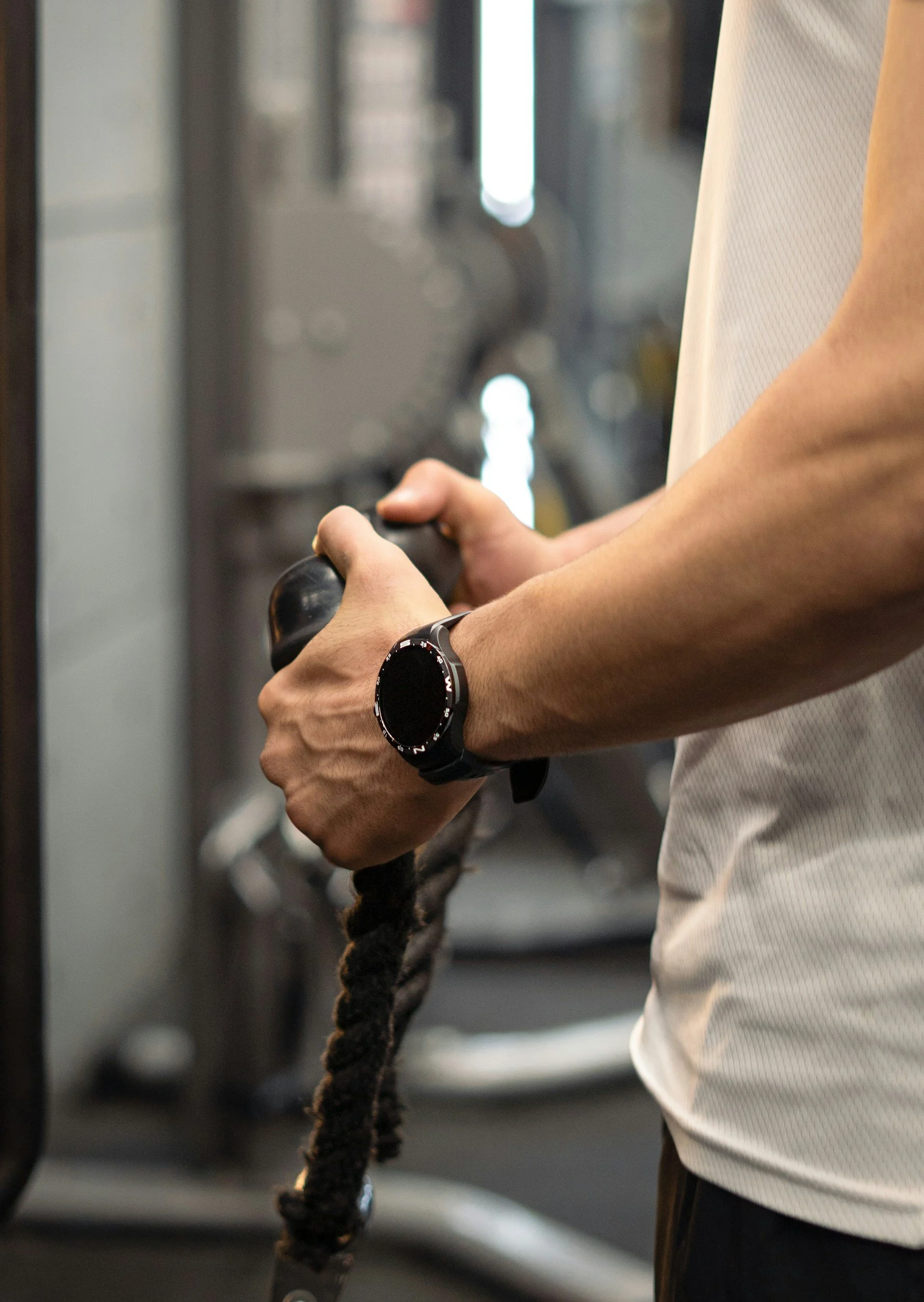 A person gripping gym equipment with both hands, wearing a watch on their left wrist, in a gym setting.
