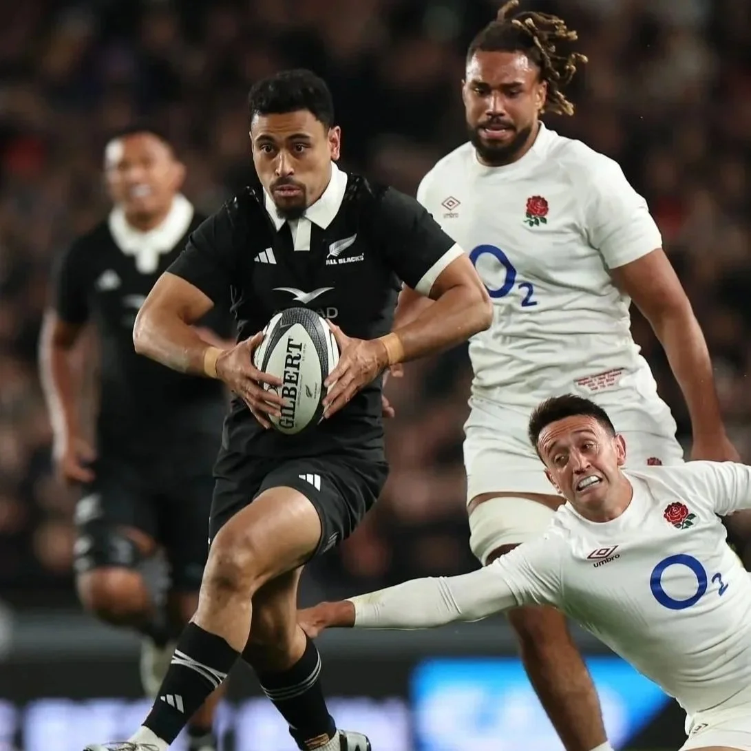 A rugby player in black uniform holding a rugby ball running away as another player in white pursuing him during a match.