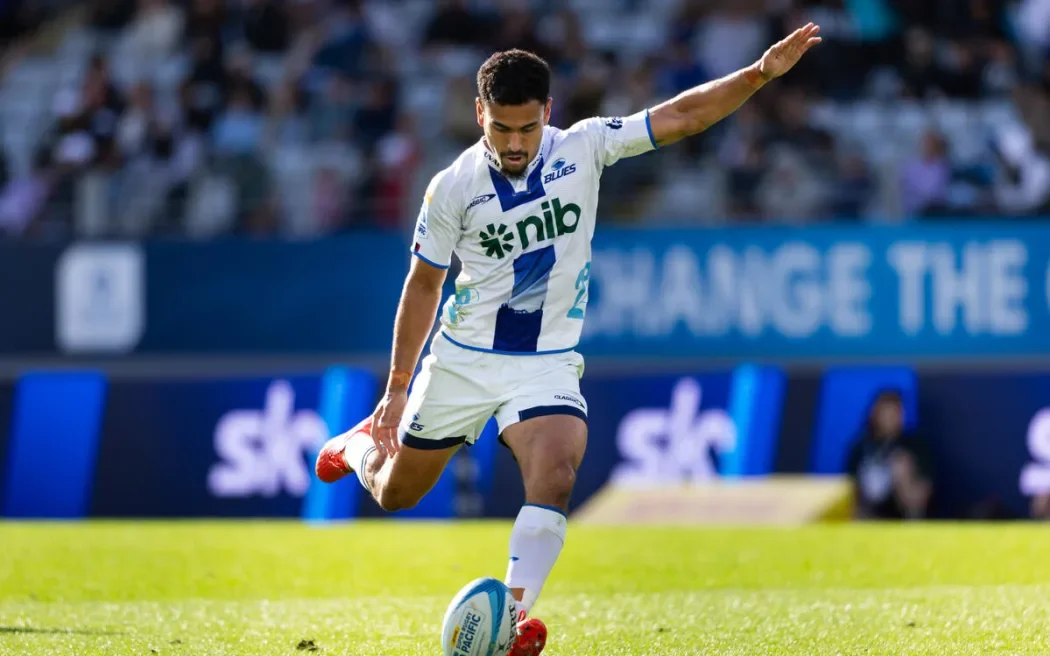 A soccer player in a white and blue jersey kicks a ball on a grass field during a match.