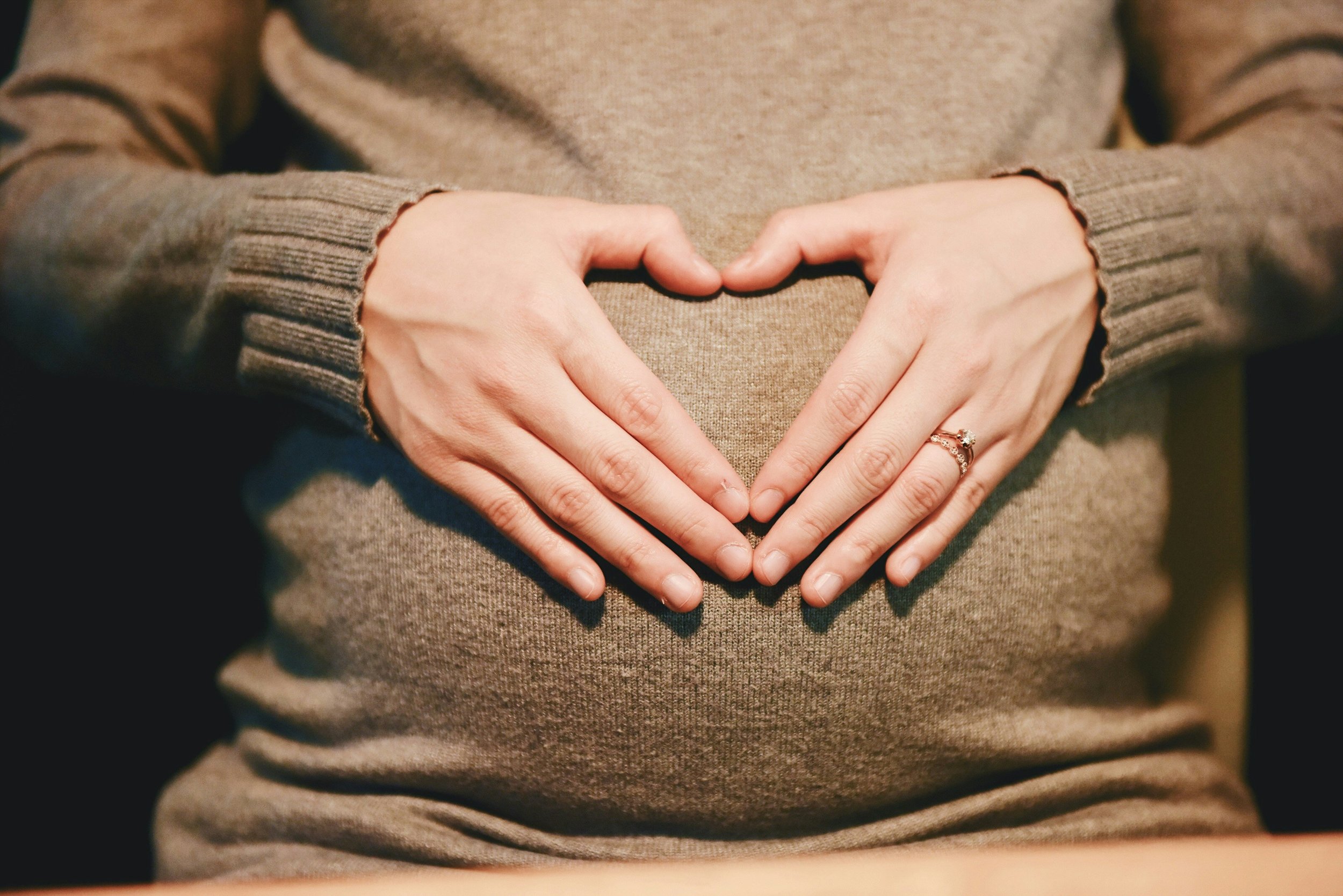Pregnant woman holding her belly forming a heart shape with hands, representing pregnancy, perinatal mental health and emotional connection