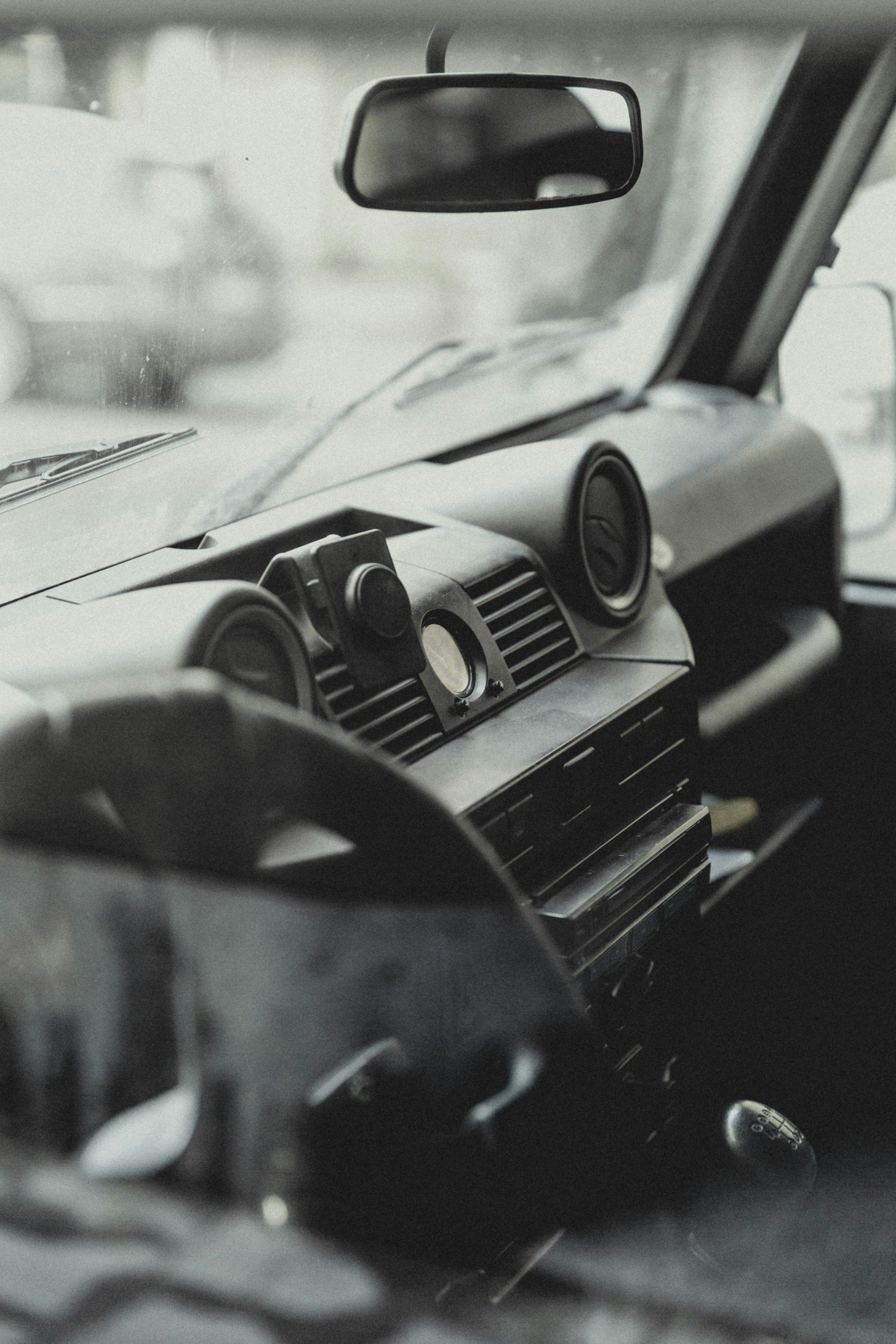 Black and white photo of a vehicle's interior, showing a dashboard with circular air vents, a central control panel, and a rearview mirror.