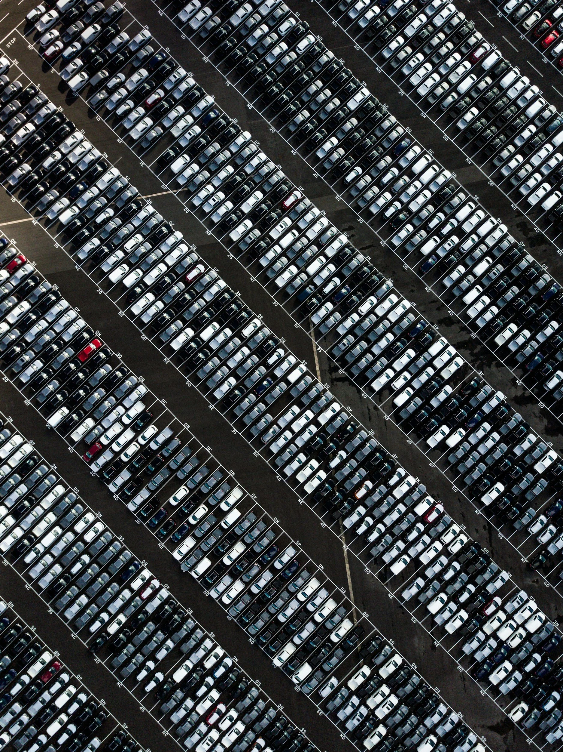 Aerial view of a large parking lot filled with numerous parked cars arranged in parallel rows.