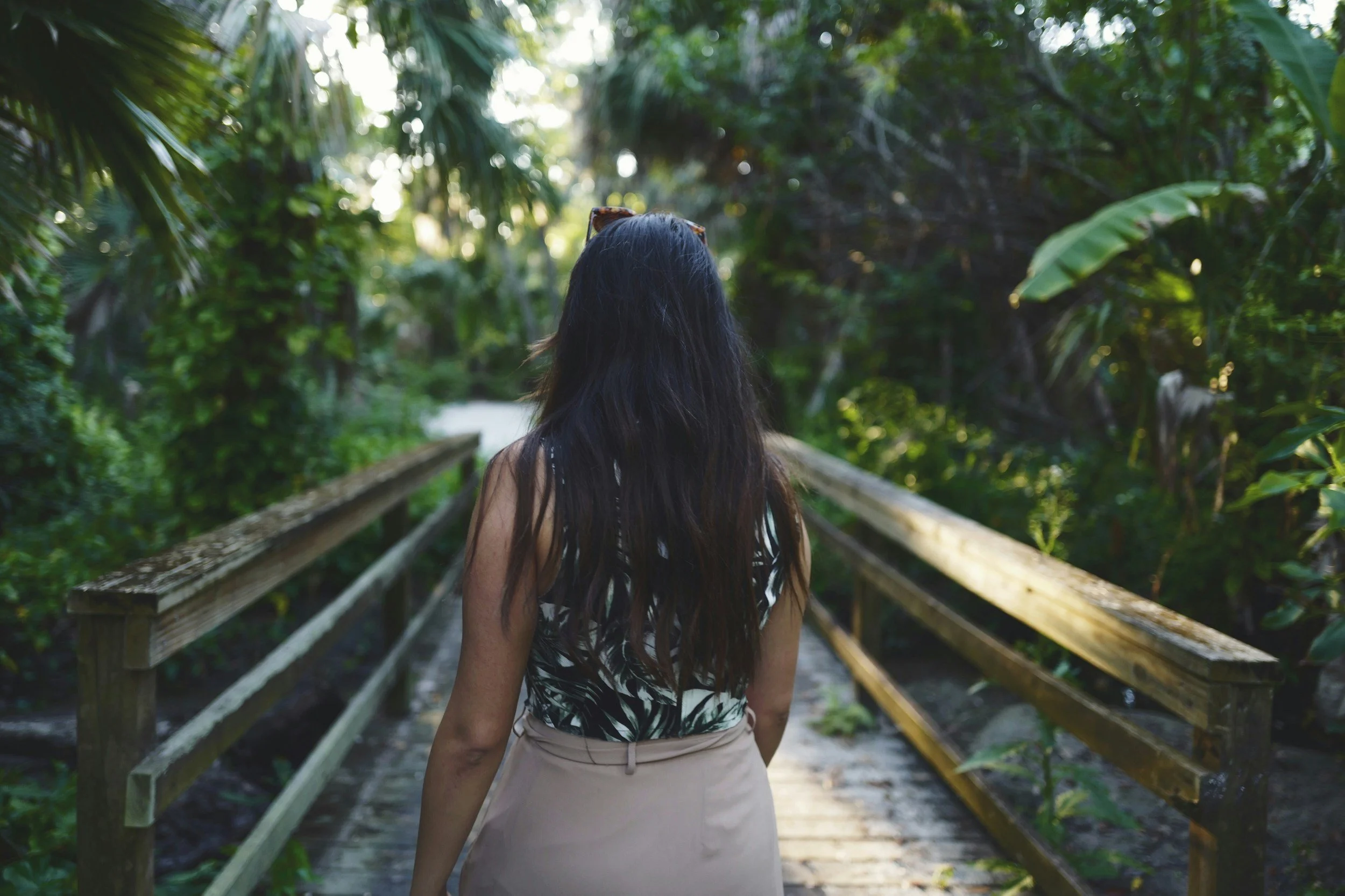 Woman walking along a wooded path surrounded by greenery, symbolizing connection and healing through nature therapy.