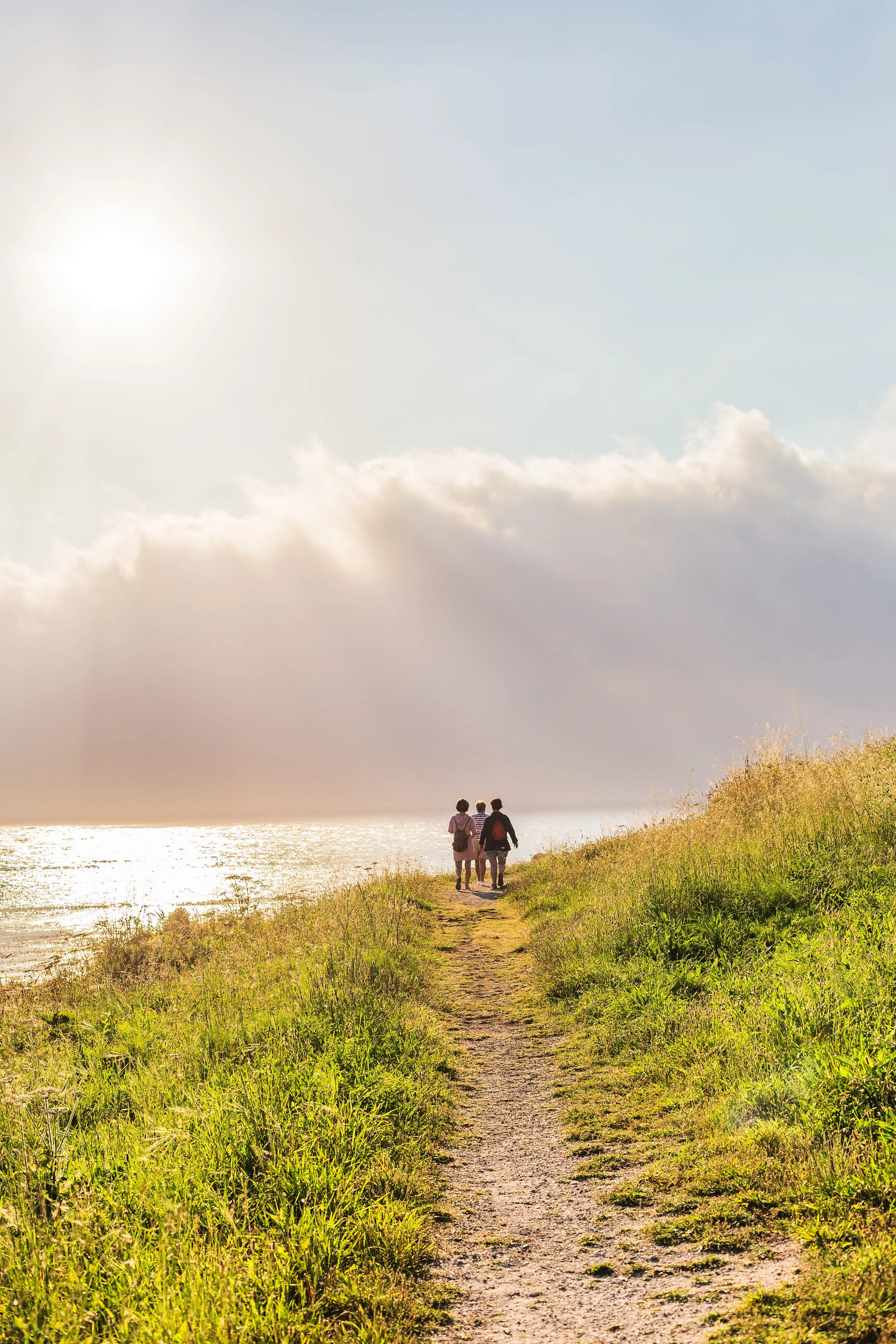 group of women walking on a sunlit coastal path surrounded by grass near the ocean, symbolizing healing and new beginnings at New Path Counseling on St. Simons Island, GA.