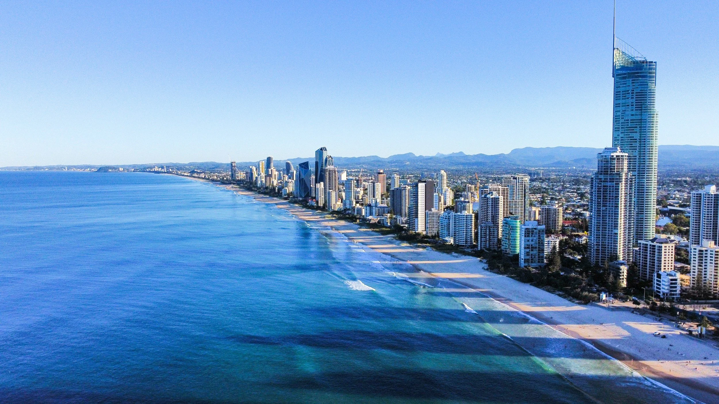 View of a city skyline along a coastline with high-rise buildings and blue ocean waves in the foreground.
