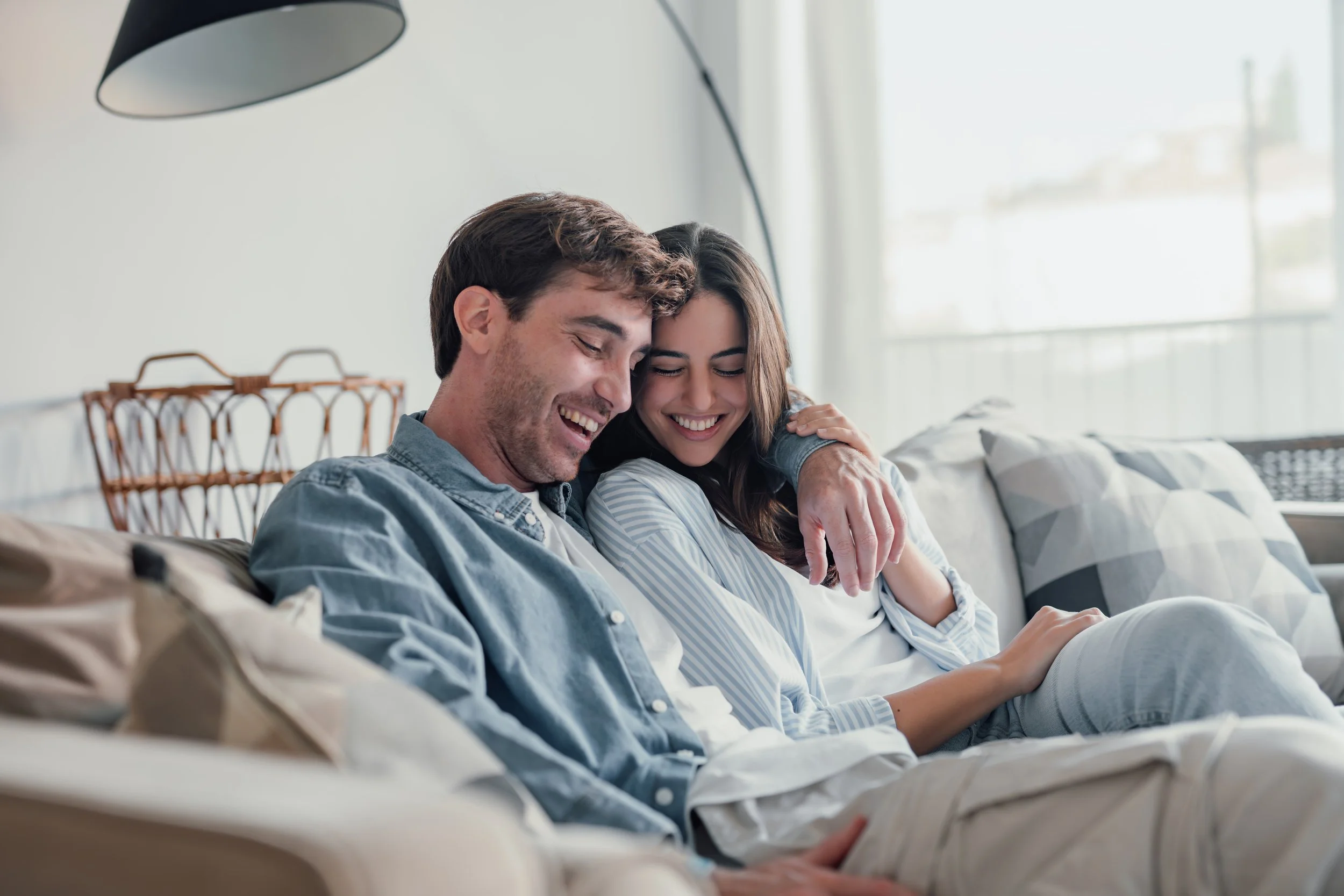A young couple sitting on a couch, smiling and sharing a happy moment together.