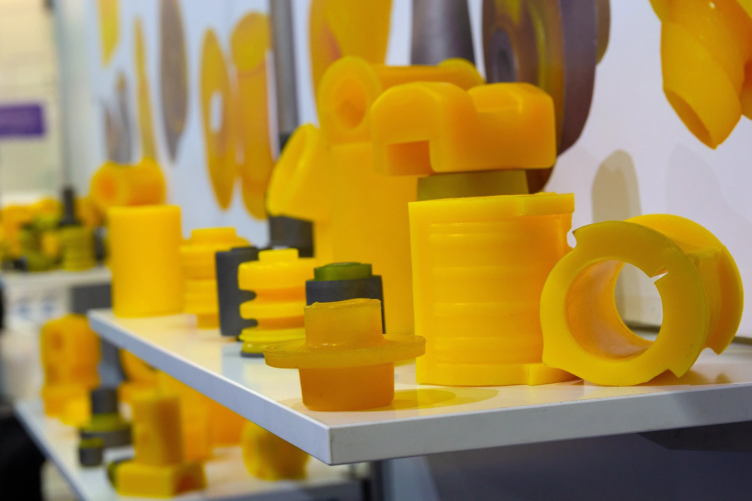 Various yellow polyurethane components displayed on a white shelf at a trade show or exhibition.