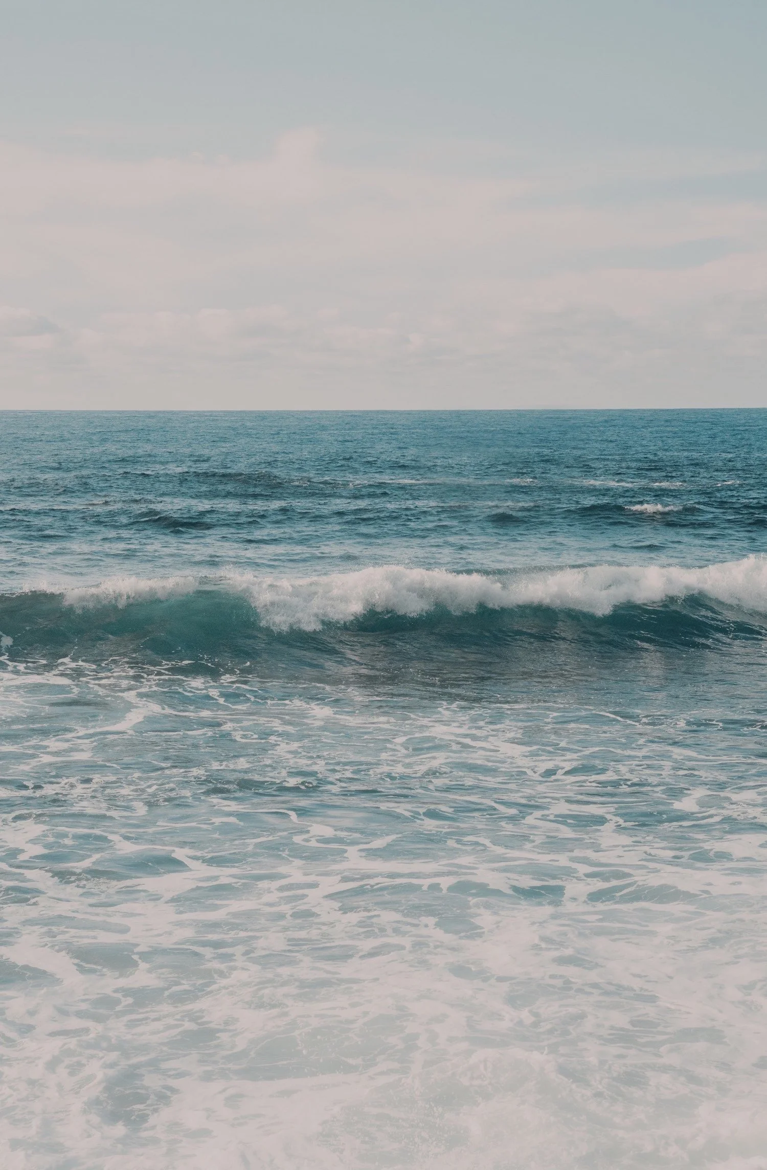 Photo of the ocean with waves and cloudy sky.