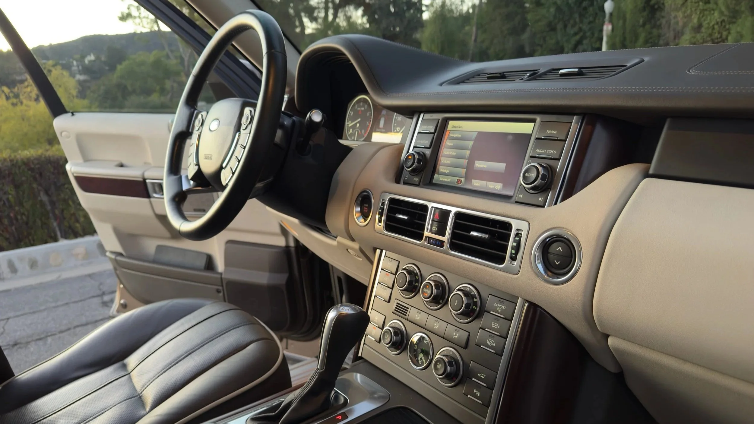 The interior of a vehicle showing the dashboard, steering wheel, gear shift, and seats, with an outdoor view visible through the windshield.
