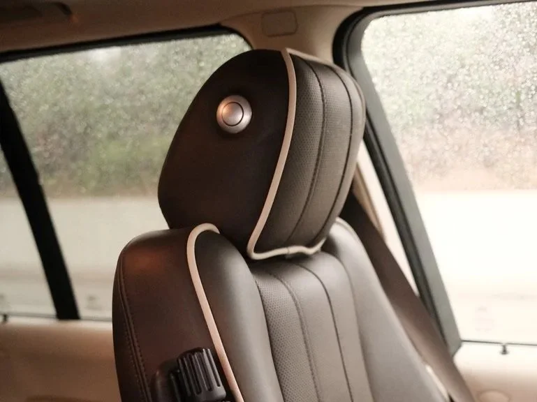 Close-up view of a black car seat with a headrest, inside a vehicle, with a window showing a blurred outdoor scene.
