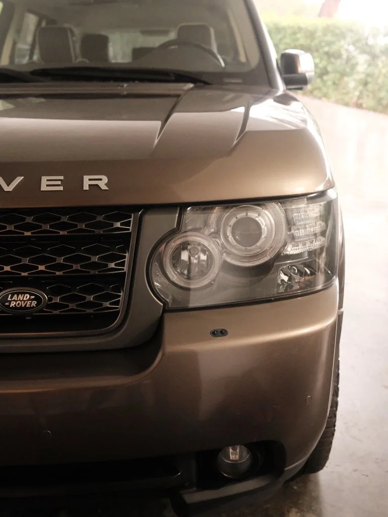Close-up of the front left side of a Land Rover vehicle, showing the headlight, grille, and part of the hood.