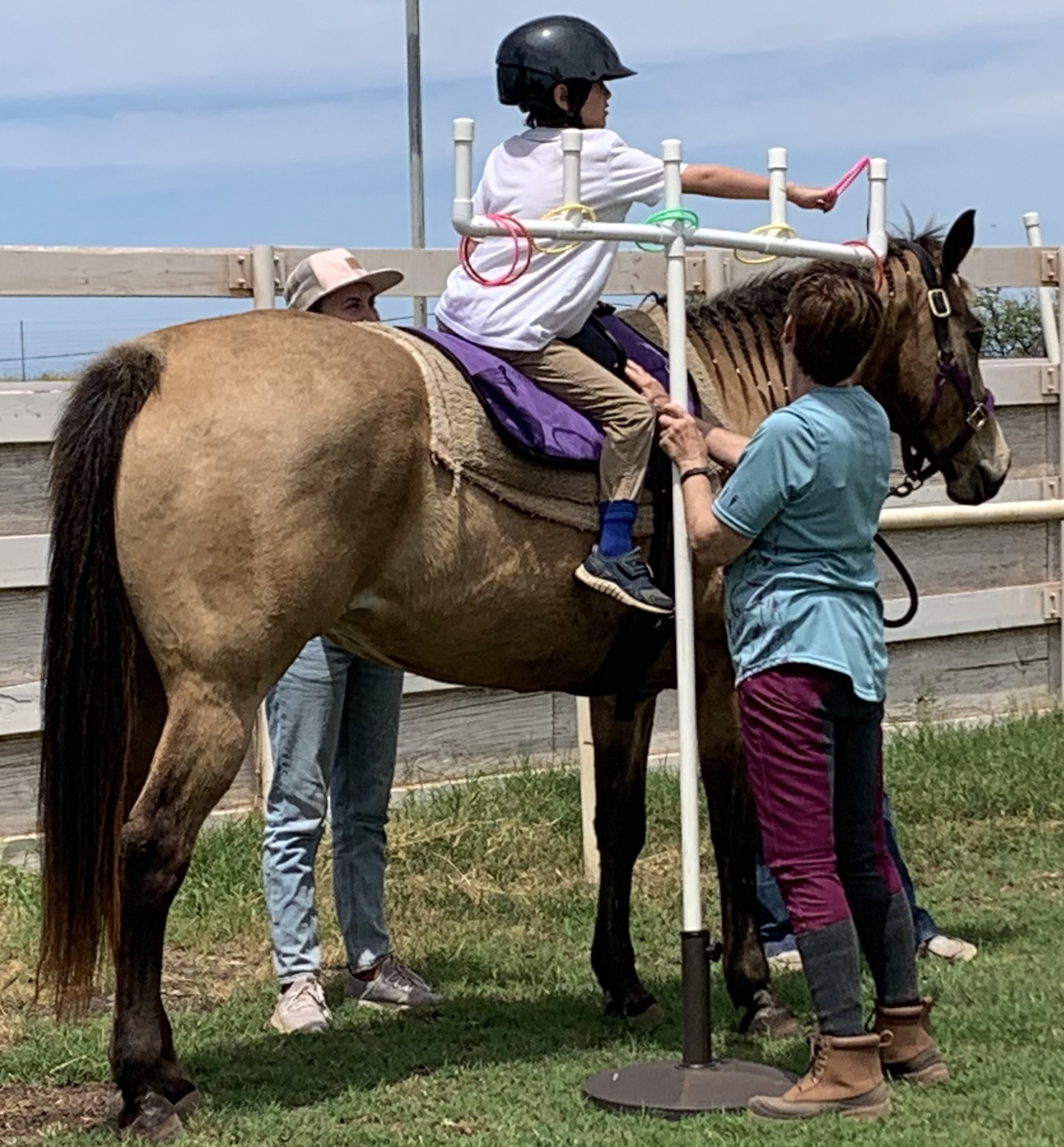Child in a helmet on a horse being assisted by two adults during a riding lesson.