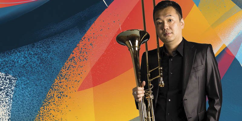 A man in a black suit holding a trumpet stands in front of a colorful abstract background. Eijiro Nakagawa,