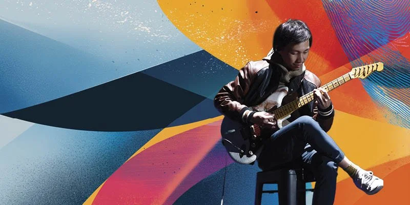 Person playing electric guitar on a stool in front of a colorful abstract background. Teriver Cheung
