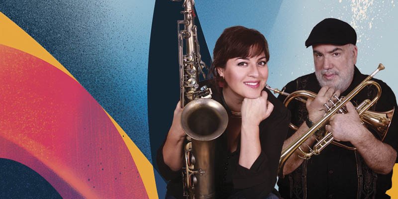 A woman and a man holding musical instruments, a saxophone and a trumpet, standing in front of a colorful abstract background.