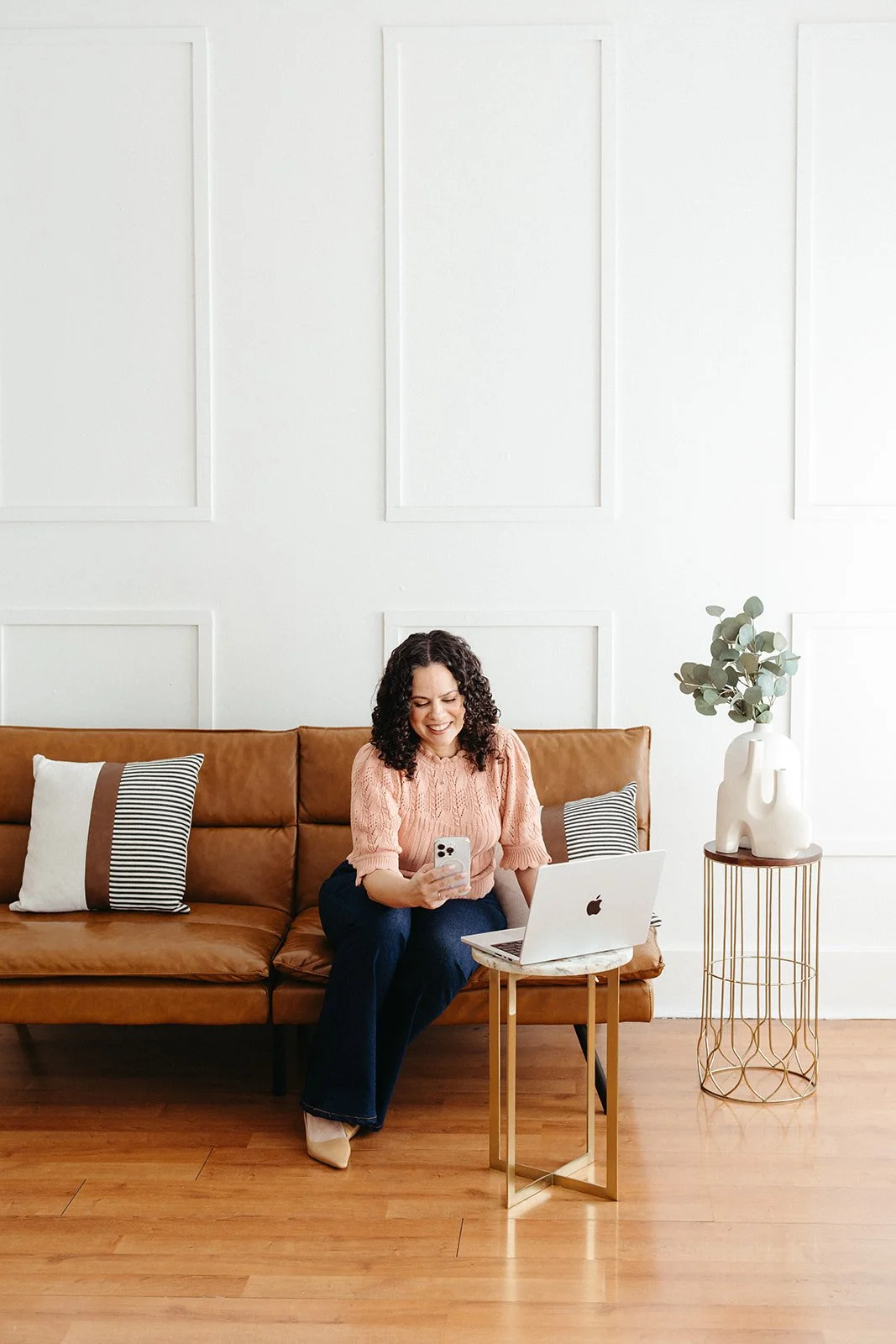 Jaclyn Staubach, LCSW, seated on a leather couch using a smartphone and laptop