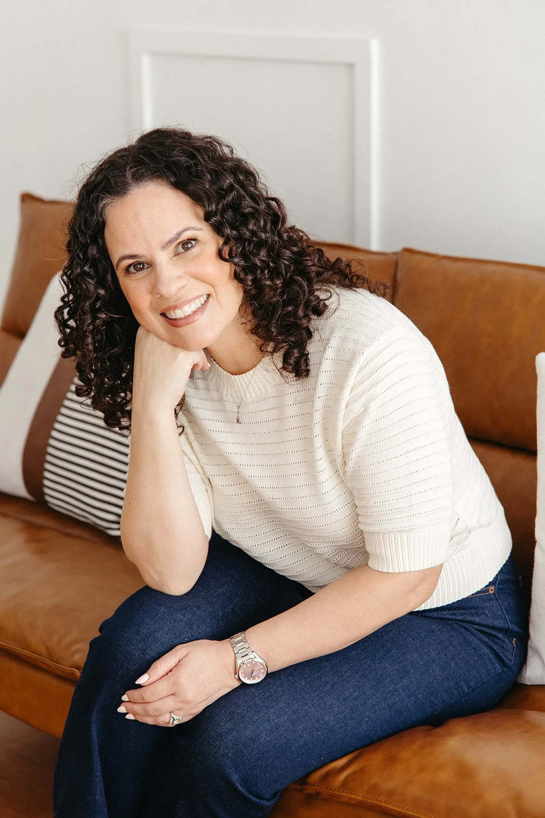 Jaclyn Staubach, LCSW, seated indoors on brown leather couch