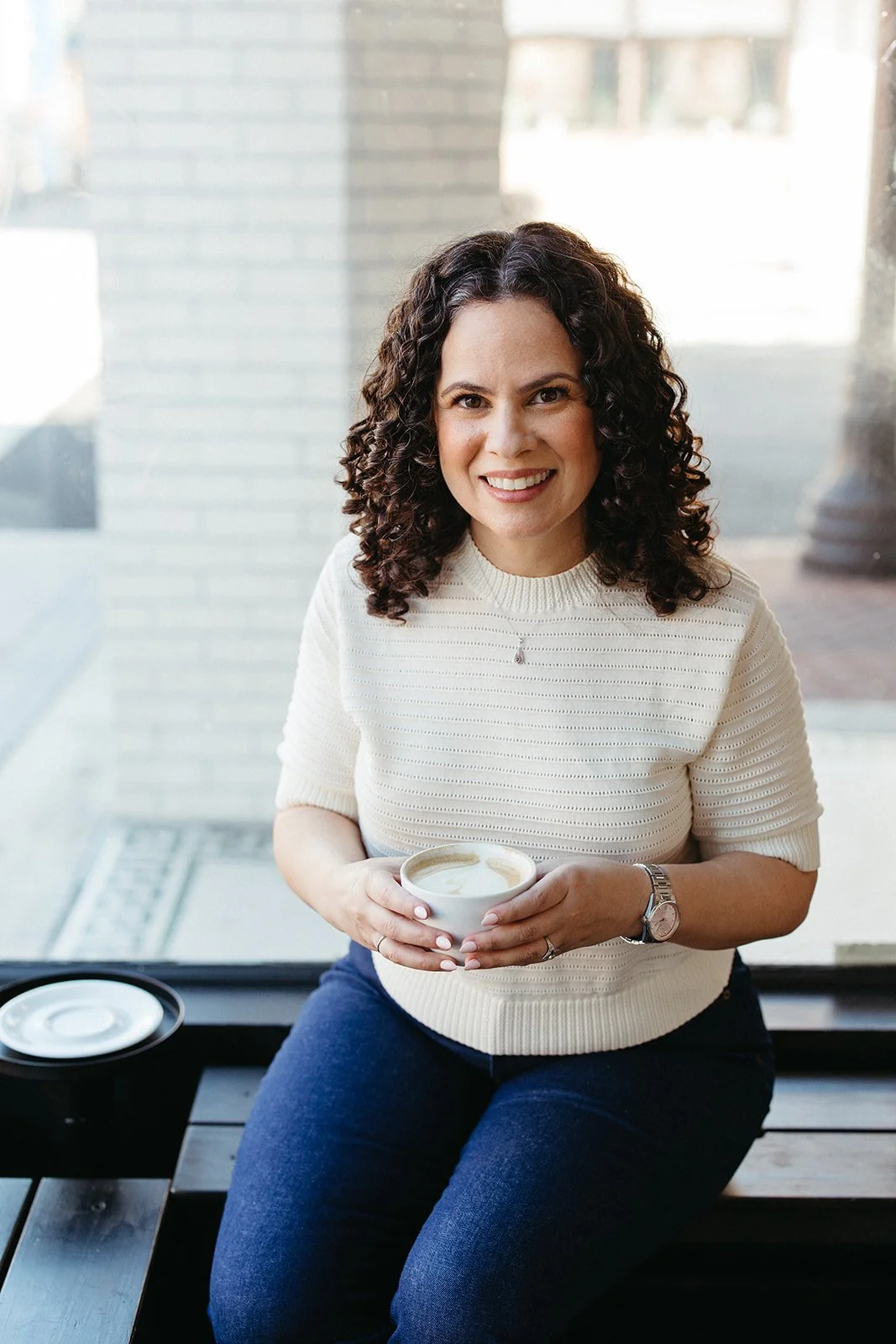 Jaclyn Staubach, LCSW, seated indoors holding a cup of coffee