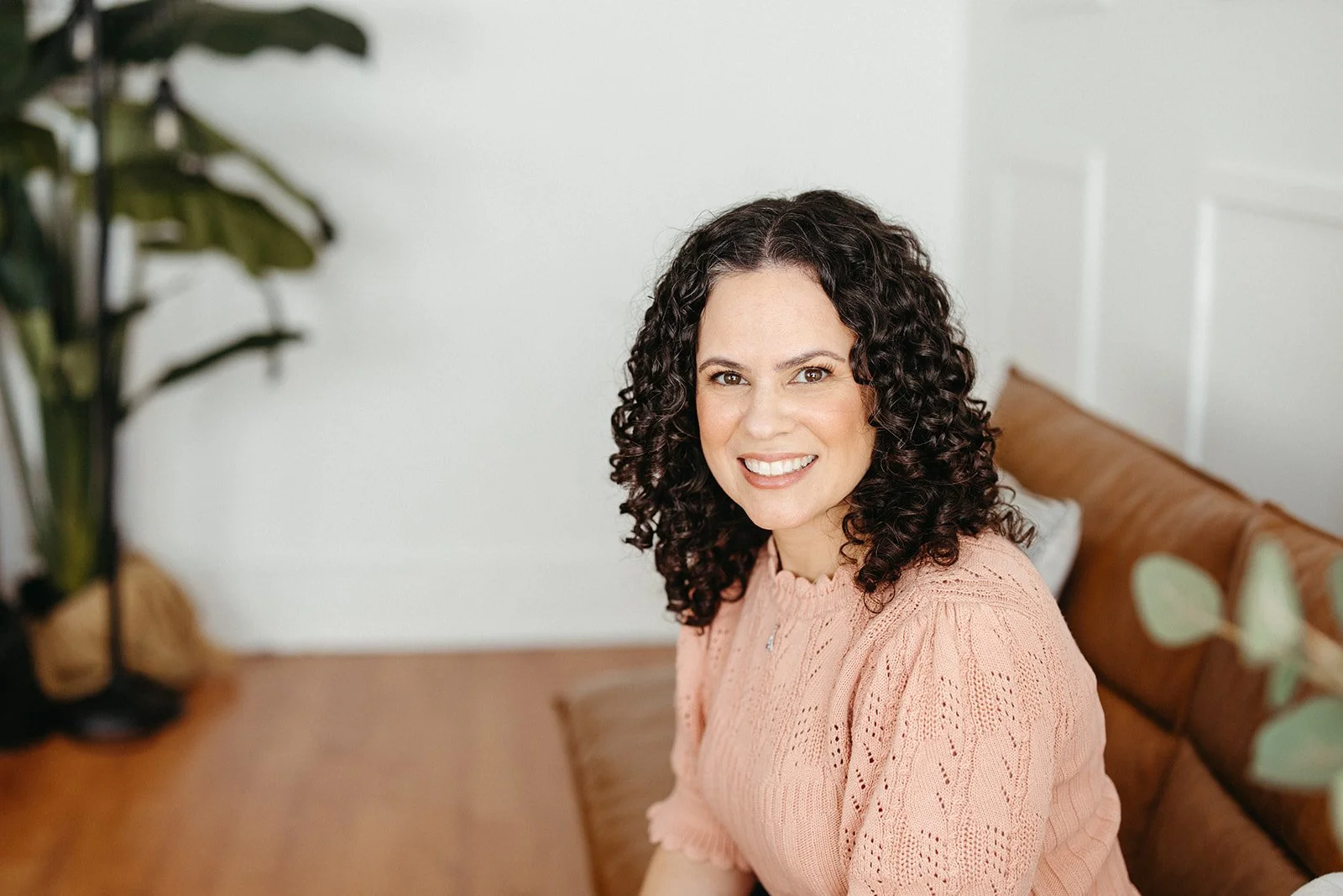 Smiling Brea, CA anxiety therapist Jaclyn Staubach, LCSW, wearing a rose shirt on a brown couch in her office.