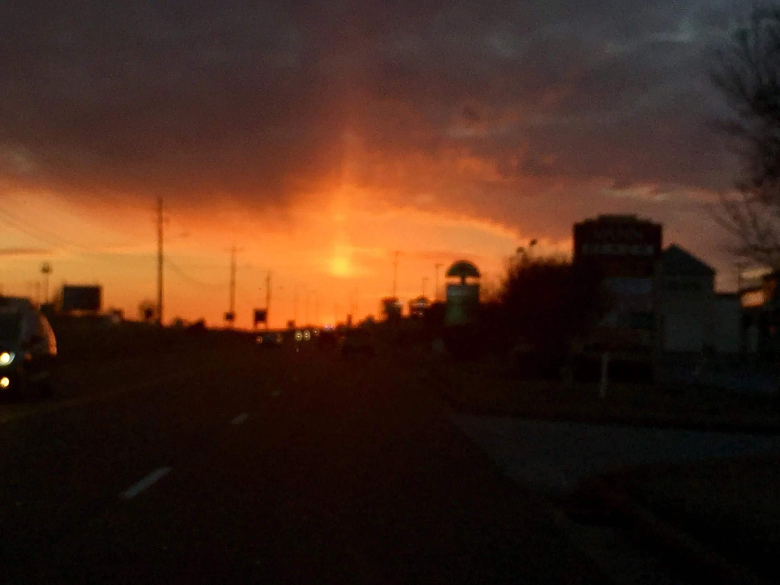 Sunset with a dramatic, fiery sky, dark clouds, and silhouettes of buildings and power lines.