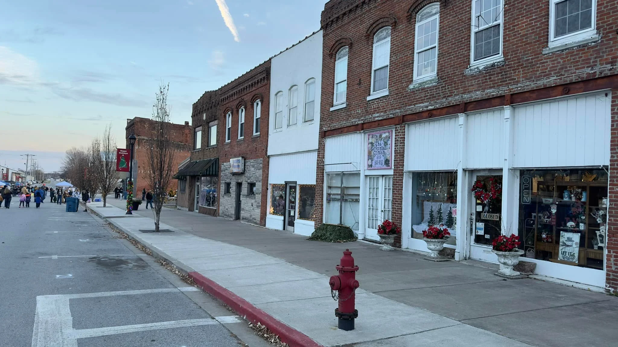 Street view with brick buildings, storefronts decorated for Christmas, and people walking on the sidewalk in a small town