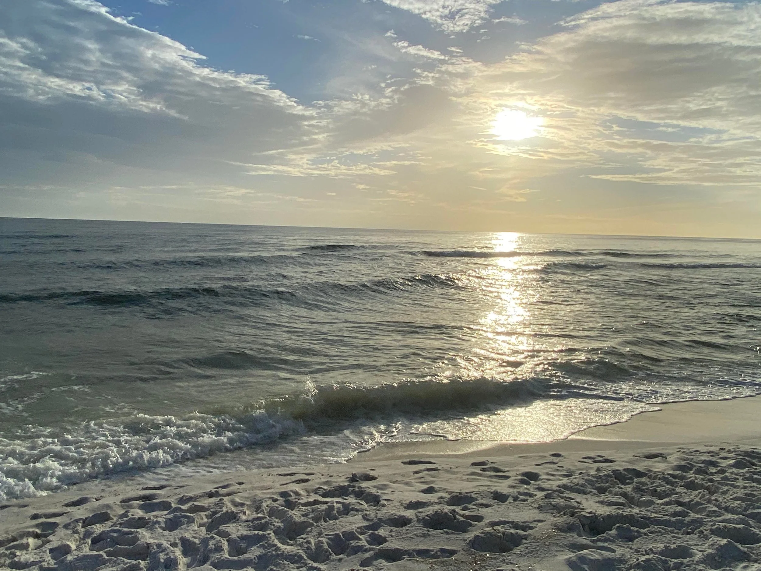 Sun setting over the ocean with waves gently crashing onto a sandy beach.