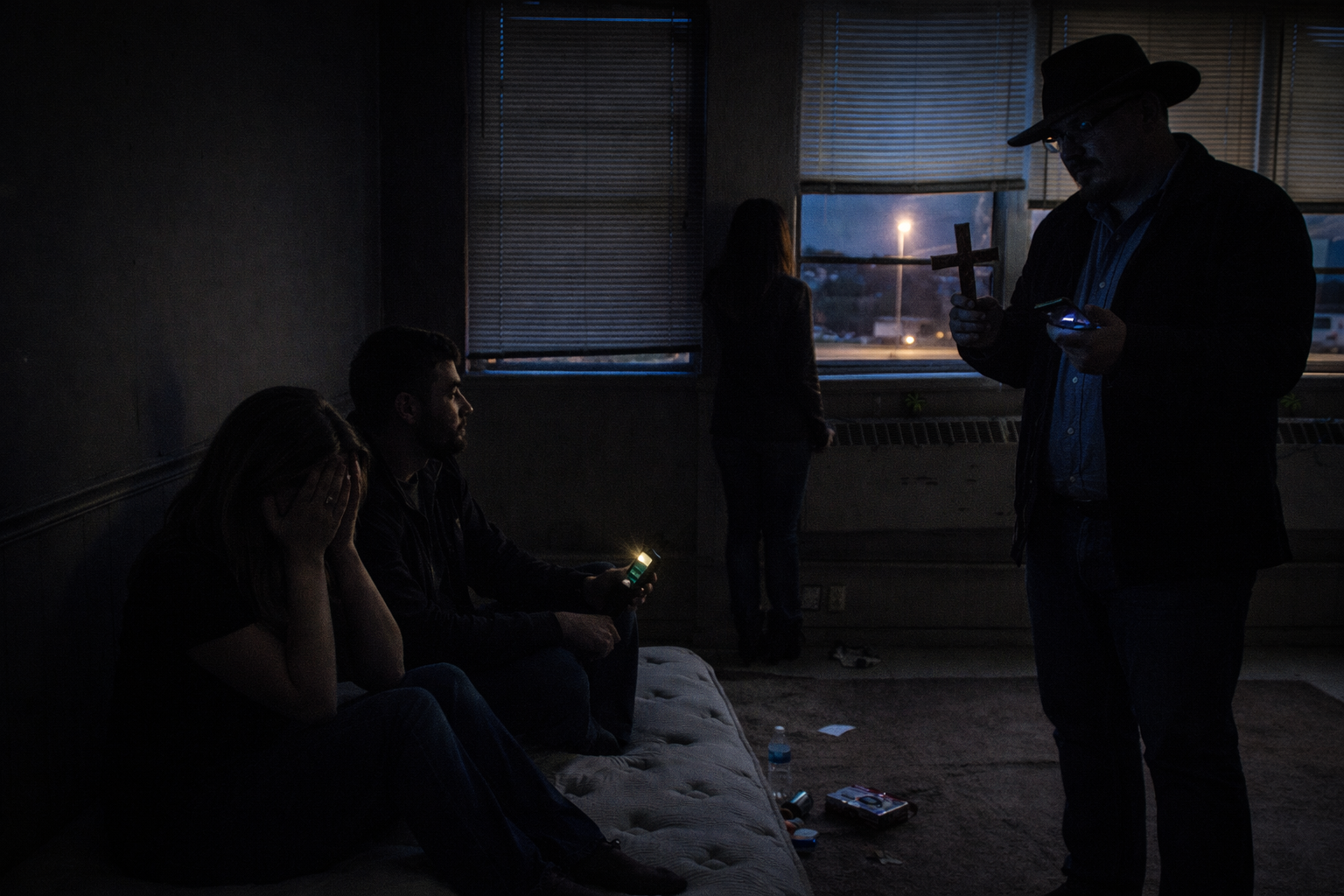 “Four paranormal investigators in a dimly lit room at dawn—one holds a cross and recorder, one watches the window, and another comforts a distressed teammate. Captures the emotional toll of spiritual warfare investigations in rural Tennessee.”