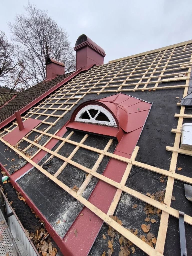 På ett tak som är under renovering ligger nya träreglar, och ett fönster är infogat i taket med en röd tätning runt.