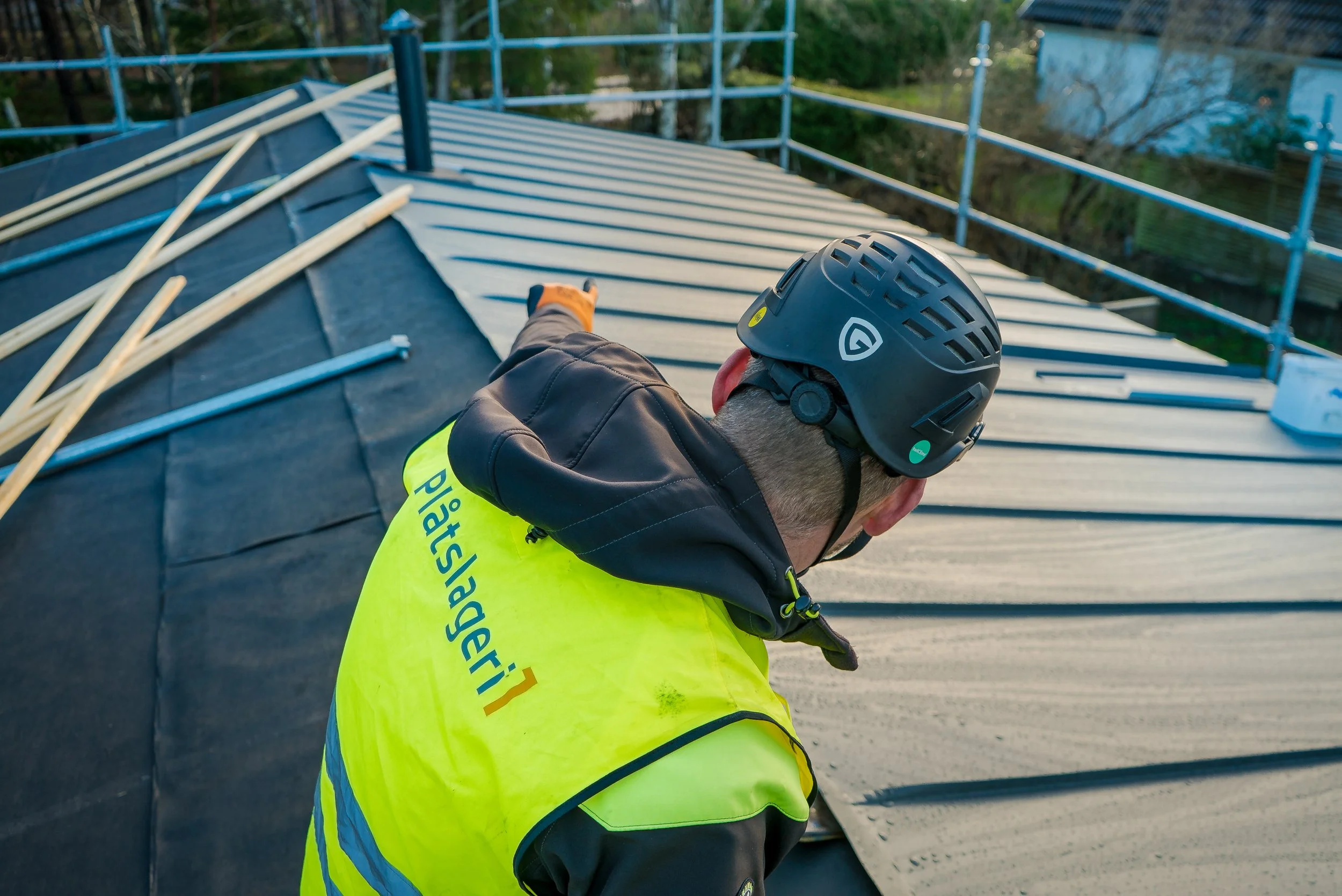 En person med hjälm och reflexväst arbetar på ett tak, som är under reparation eller byggnation.