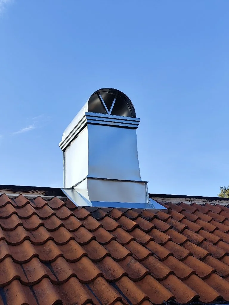 En takfönster med ett metallkåpa på ett tegelpannat tak under en klar blå himmel.