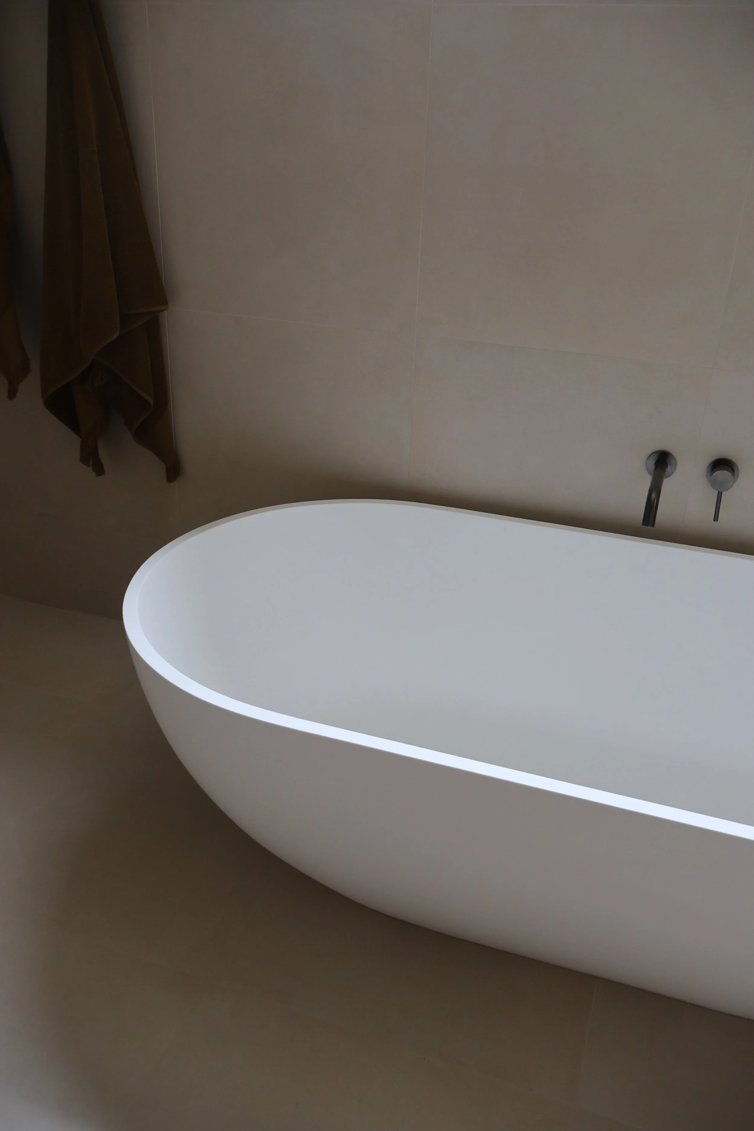 Modern white freestanding bathtub in a bathroom with beige walls and floor.