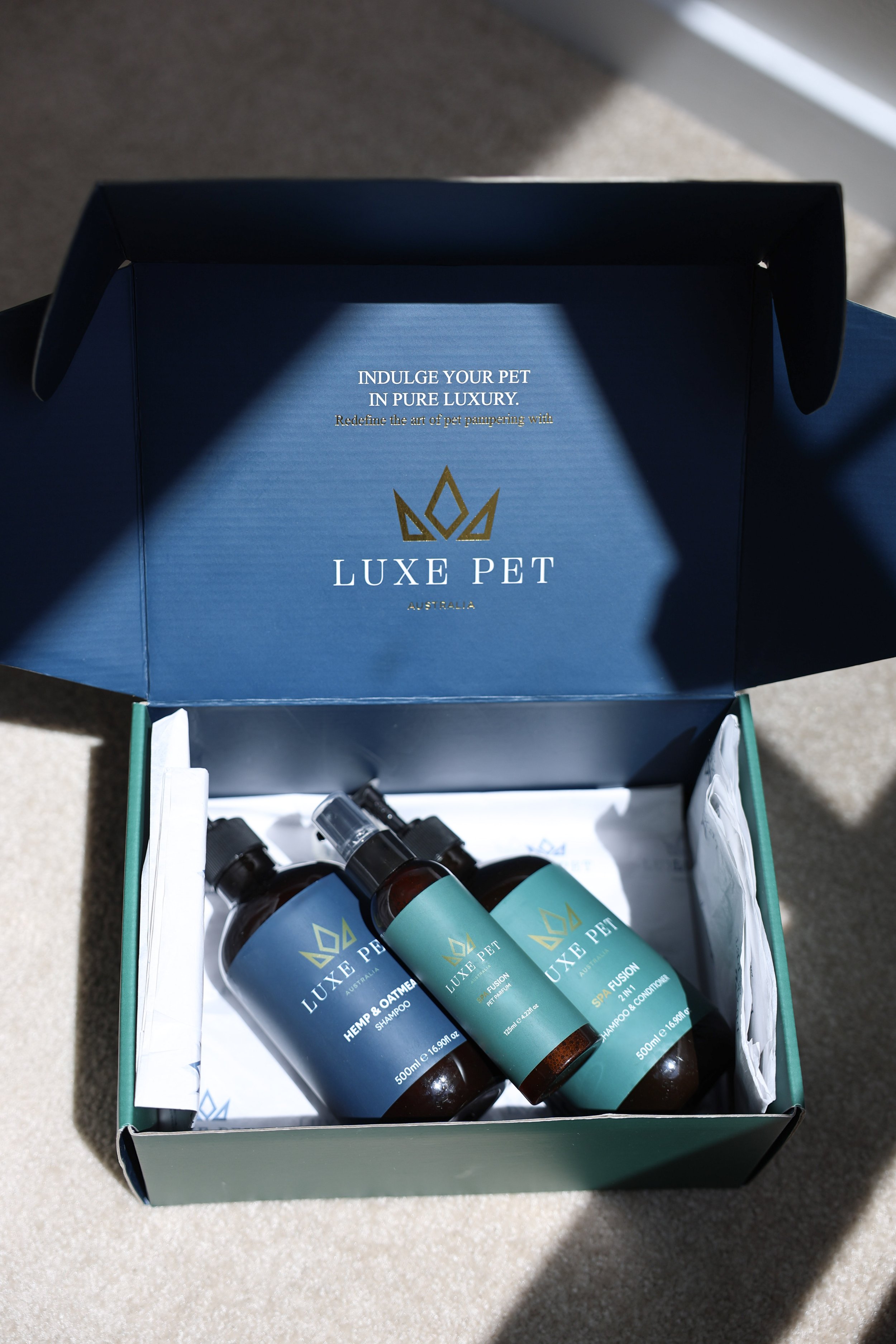 Open Luxe Pet box containing three bottles of pet grooming products on a light-colored carpet.