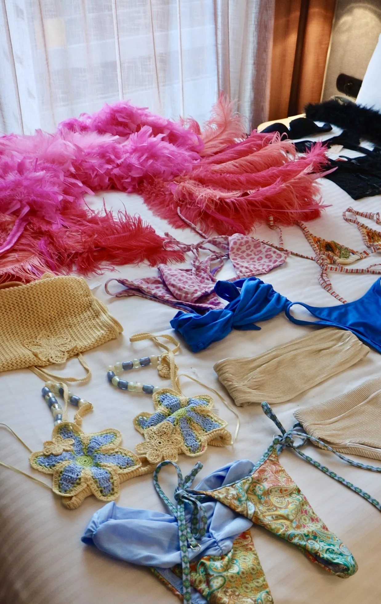 Colorful feather boas, bikinis, crocheted accessories, and other clothing items laid out on a bed.