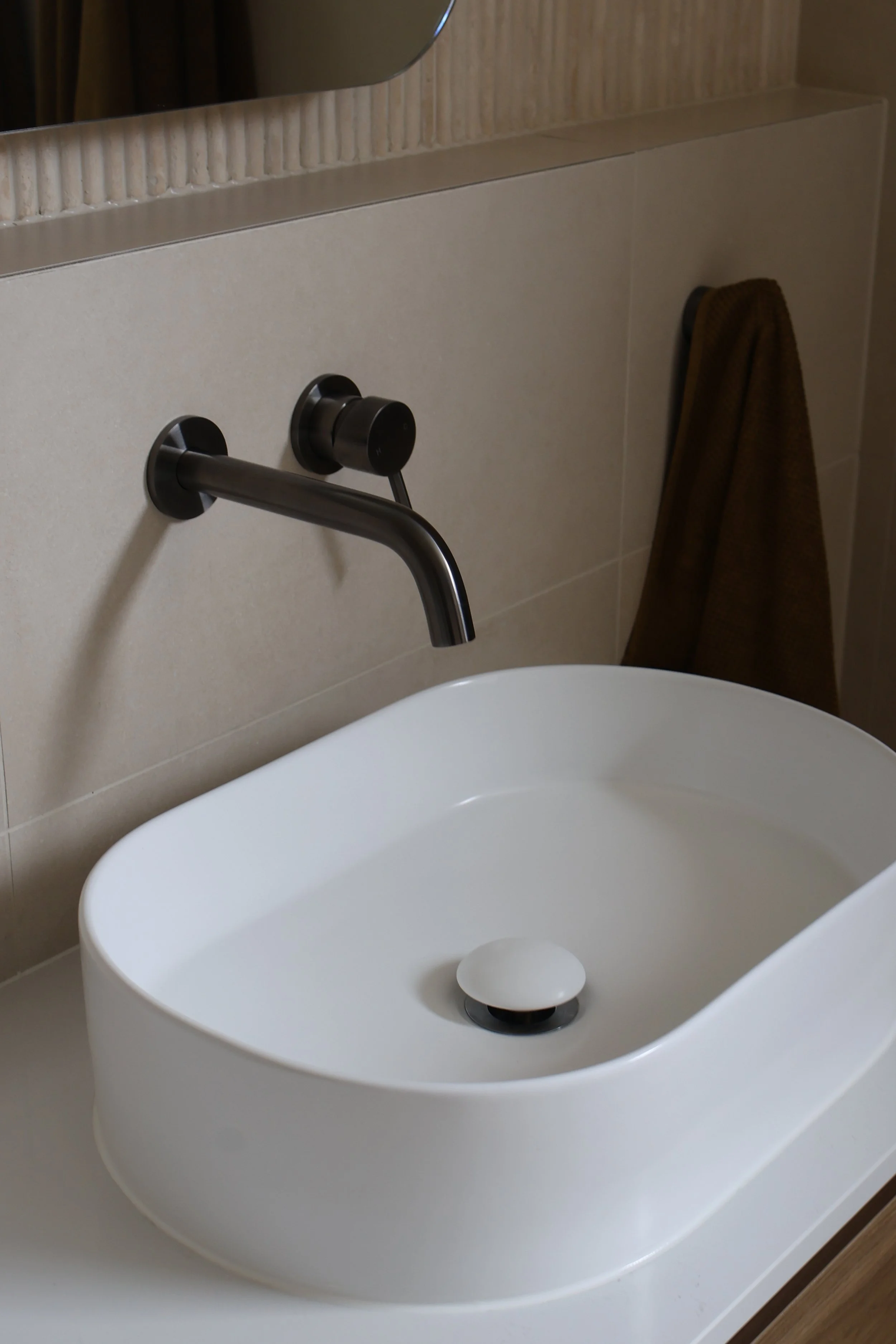 Modern bathroom sink with a sleek, black wall-mounted faucet and a brown towel hanging nearby.