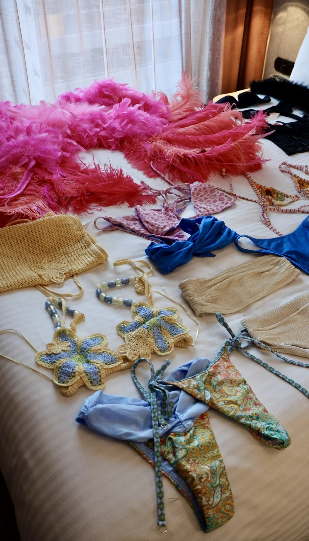 A bed covered with various colorful swimsuits, bras, necklaces, and feather boas.