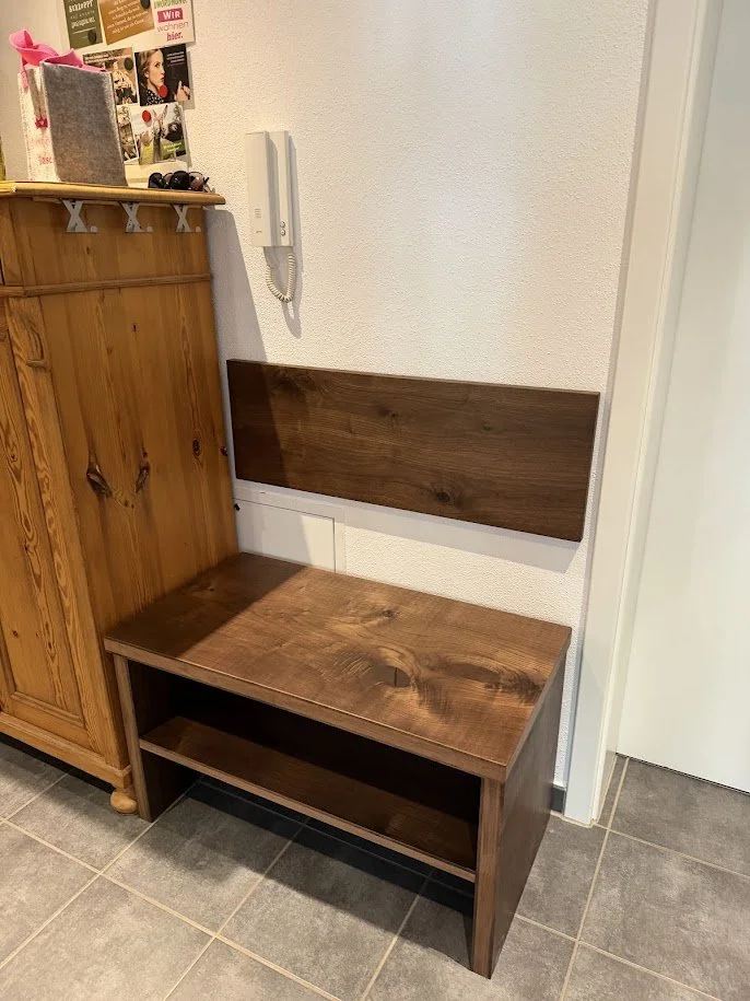 Ein selbstgebautes Holzbank mit Rückenlehne und Ablage darunter, an einer Wand neben einer Holzschrank