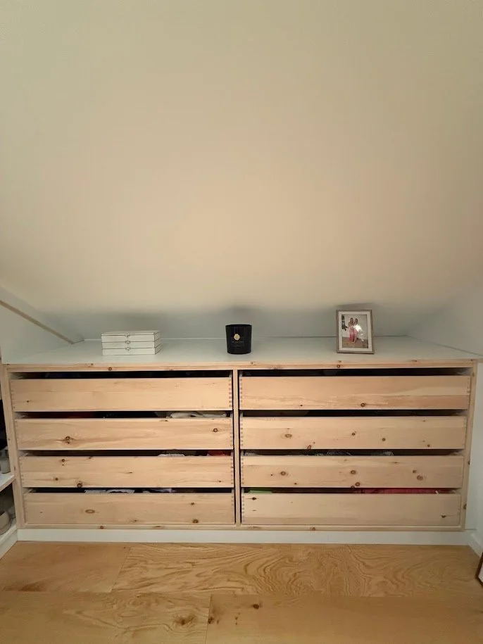 Holzkommode mit je drei Schubladen, drauf sind ein Stapel weißer Bücher, eine schwarze Kerze und ein Foto in einem Rahmen.