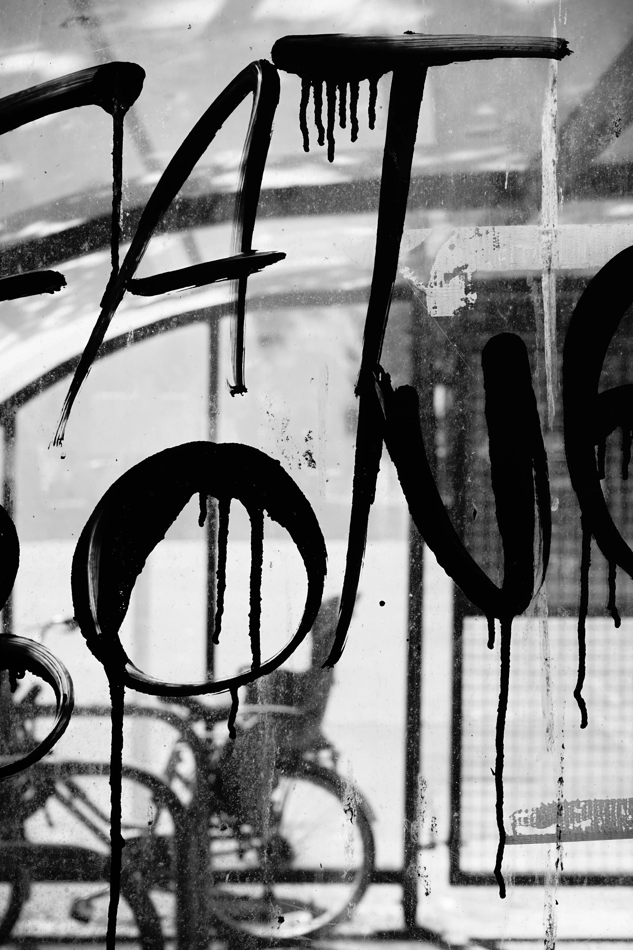 Black graffiti on a dirty glass window, with visible outlines of bicycles behind the glass.