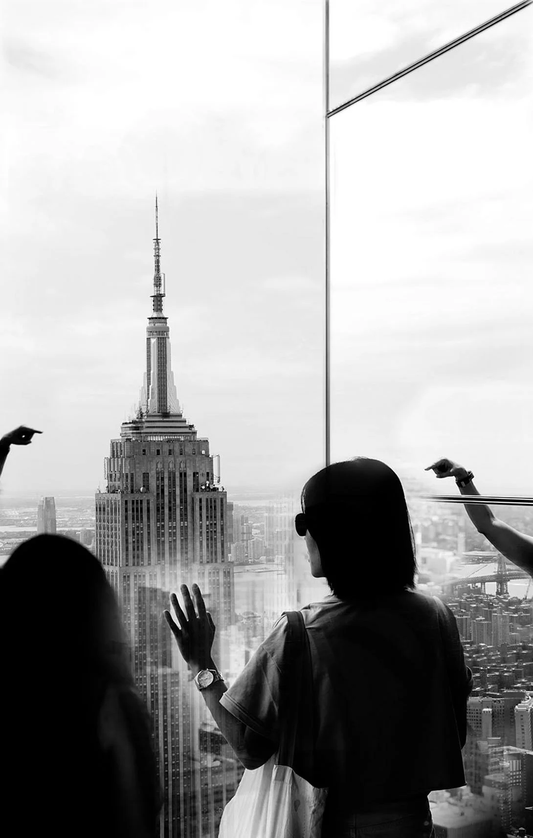 Black and white photo of people looking at the Empire State Building from a high-rise observation deck.