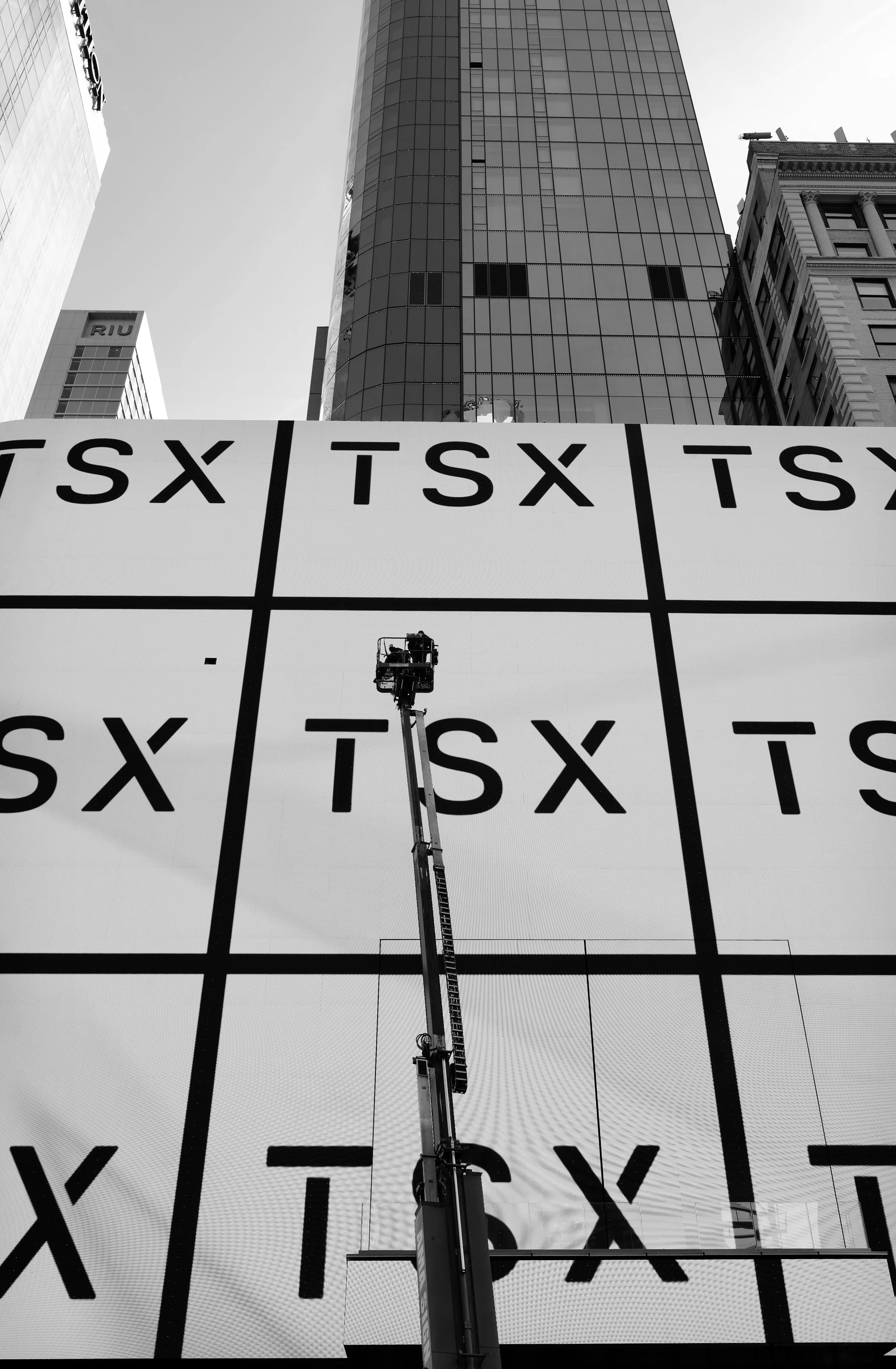 Workers on a lift installing or maintaining a large electronic billboard in an urban city with tall buildings.