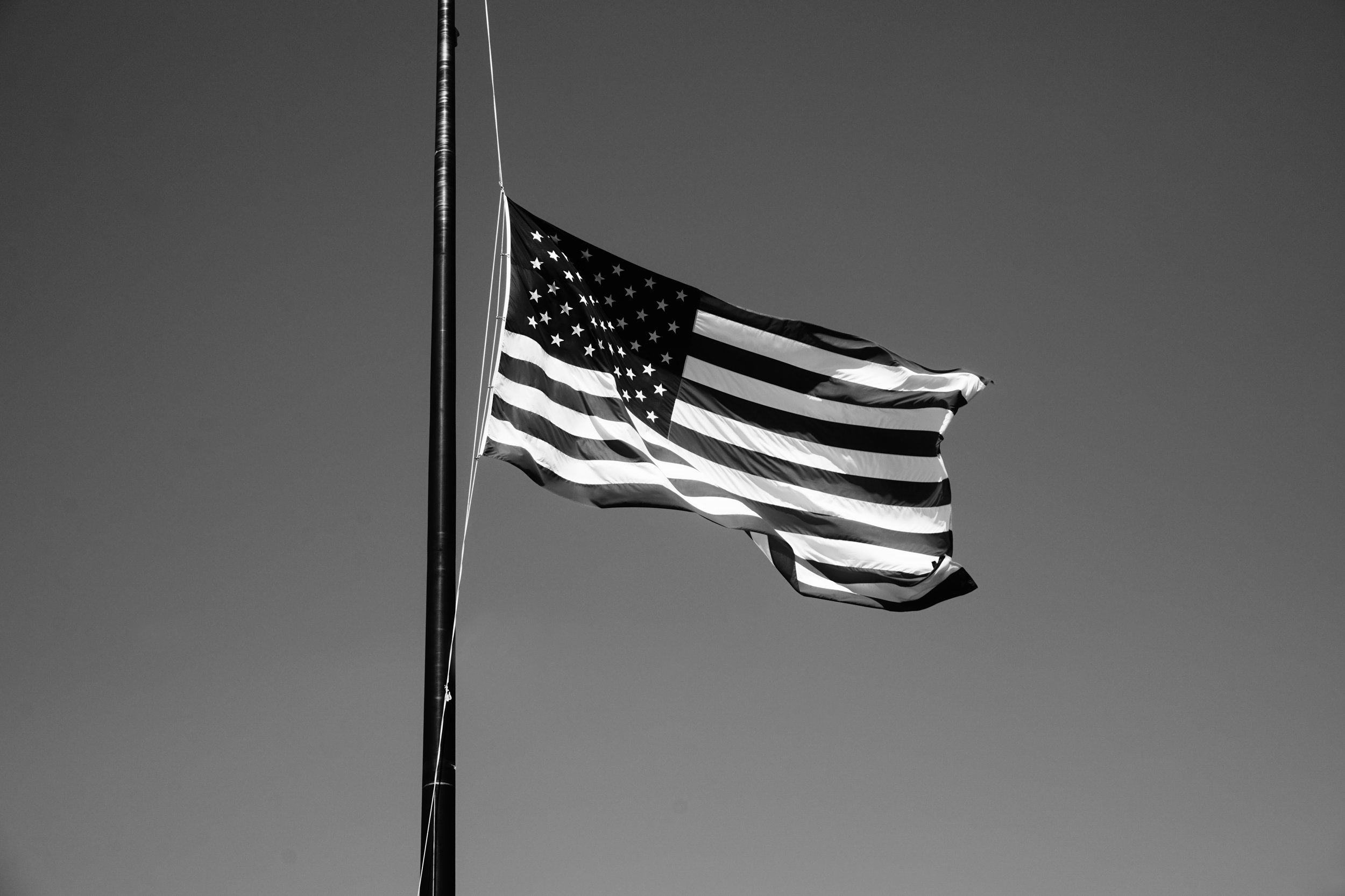 Black and white image of the American flag waving on a flagpole against a clear sky.